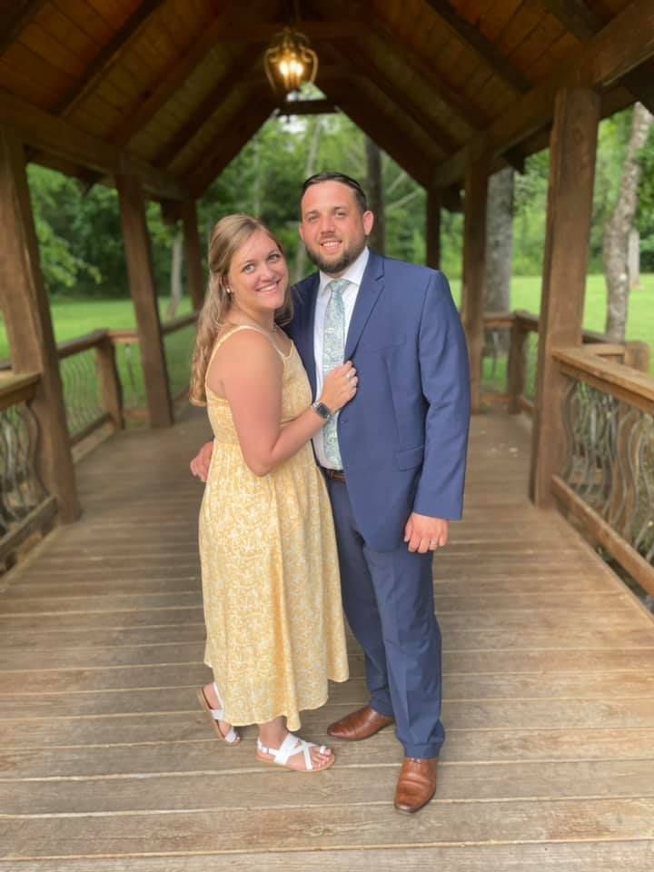 A smiling couple poses together on a wooden footbridge under a covered walkway.