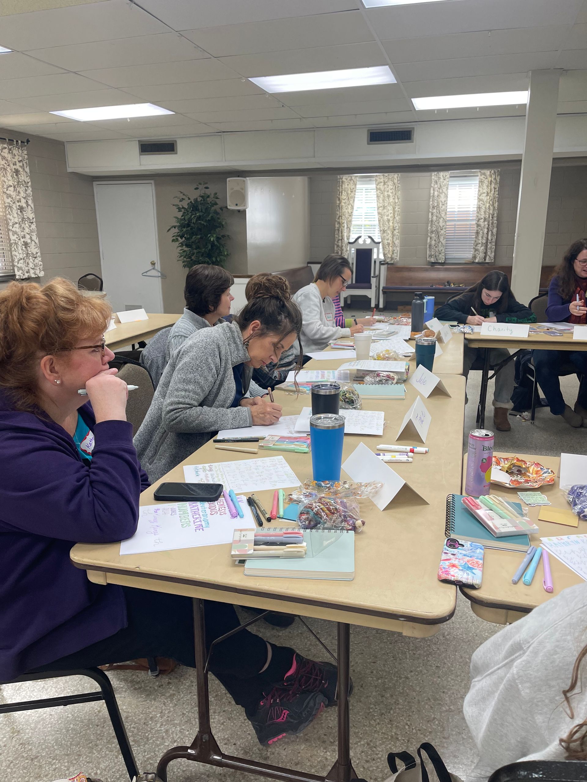 People seated at tables in a brightly lit room participating in a workshop or class.