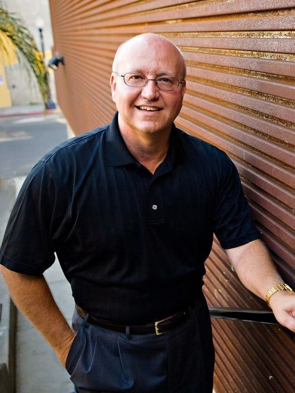 A man wearing glasses and a black shirt is leaning against a wall