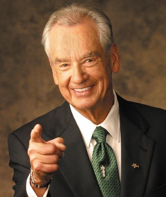 A man in a suit and tie is pointing at the camera