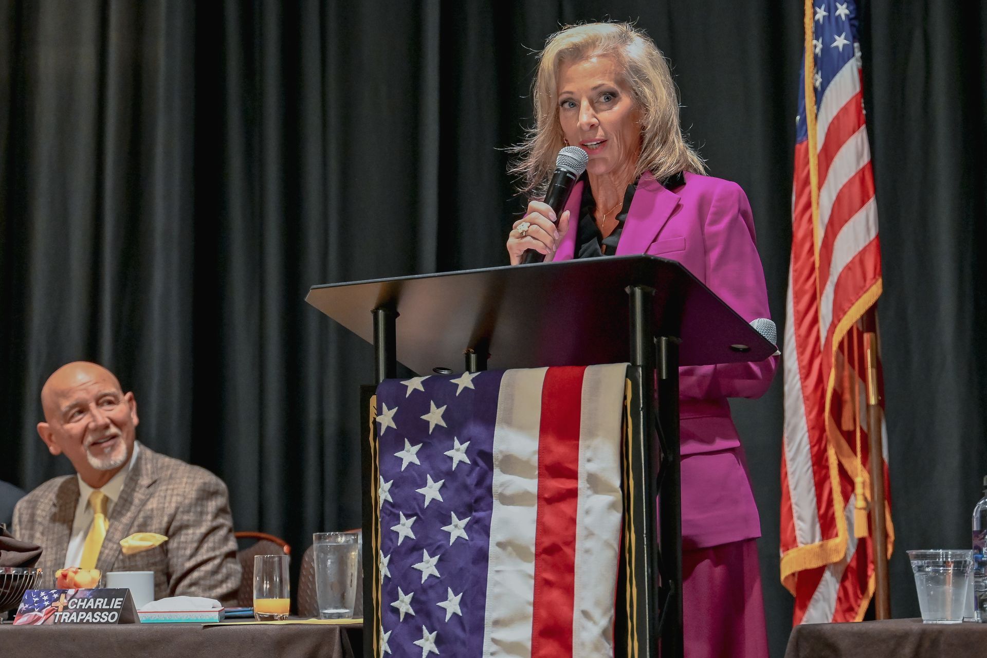 Charlie Trapasso is standing at a podium speaking into a microphone.
