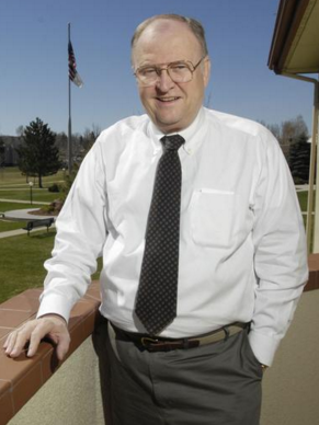 A man in a white shirt and tie stands on a balcony