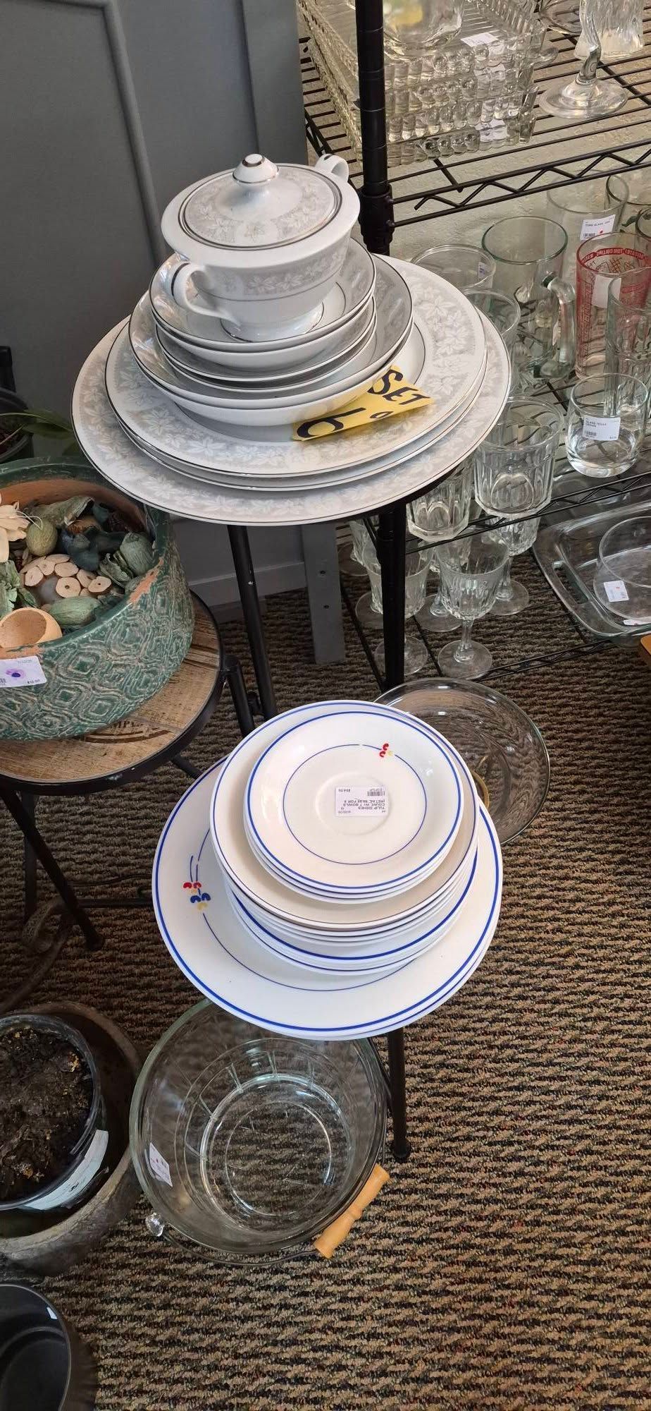 Stacked white ceramic plates and bowls displayed on a black metal table in a store.