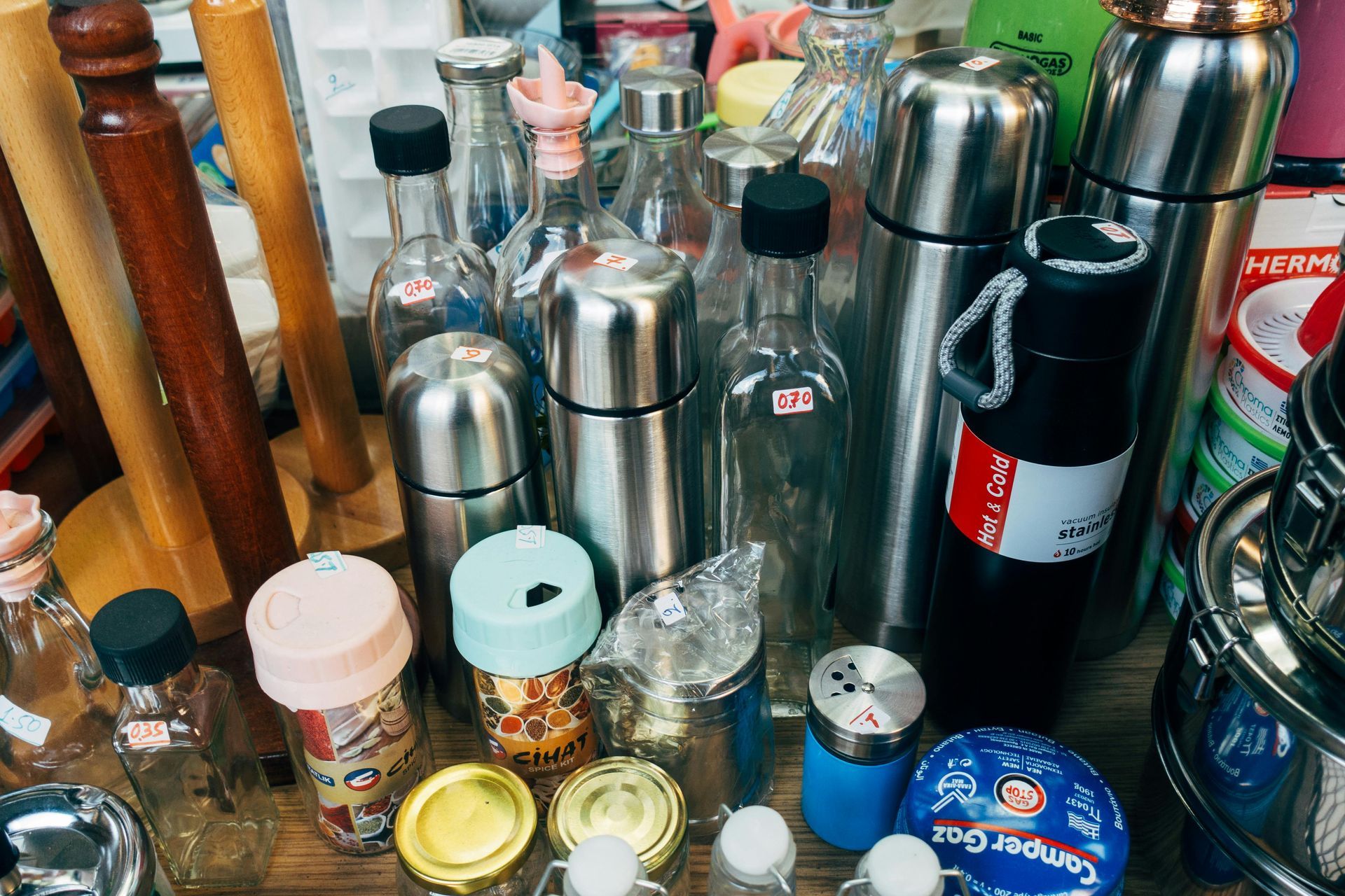 Assorted stainless steel bottles, jars, and cans clustered on a tabletop in a kitchen or pantry area