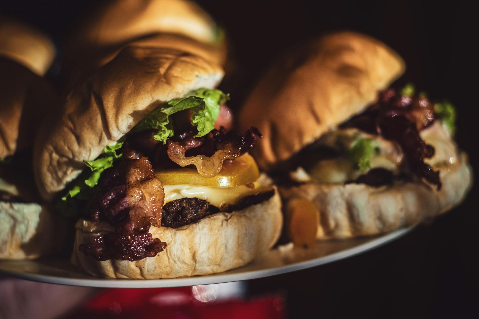 Three gourmet burgers with lettuce, cheese, and bacon on a plate