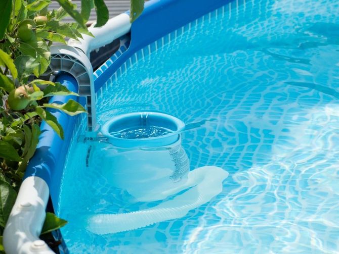 Blue pool skimmer filter in a backyard pool, with rippling clear water and leafy branches nearby
