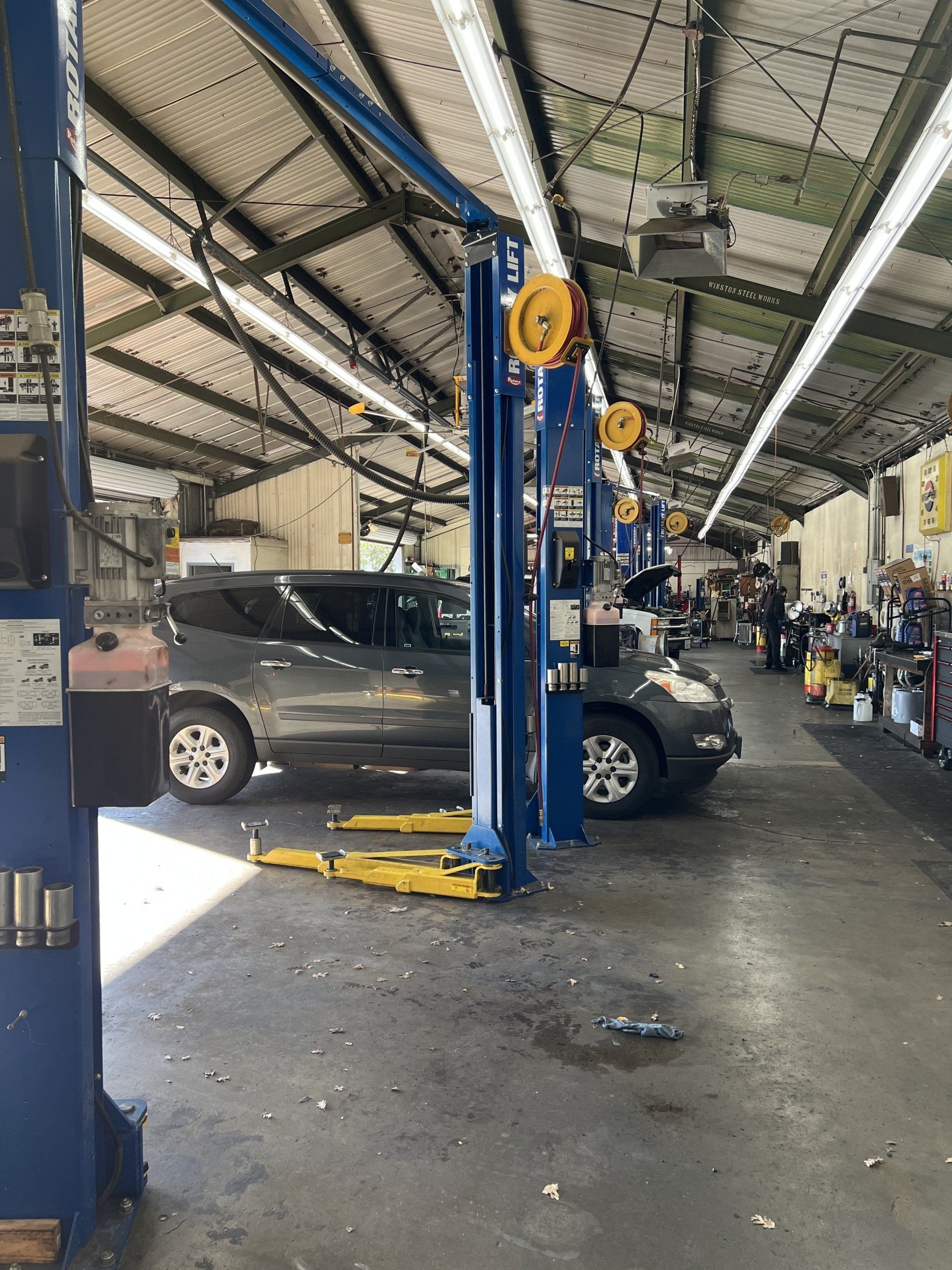 Auto repair shop with cars on lifts and mechanics working under a high industrial ceiling