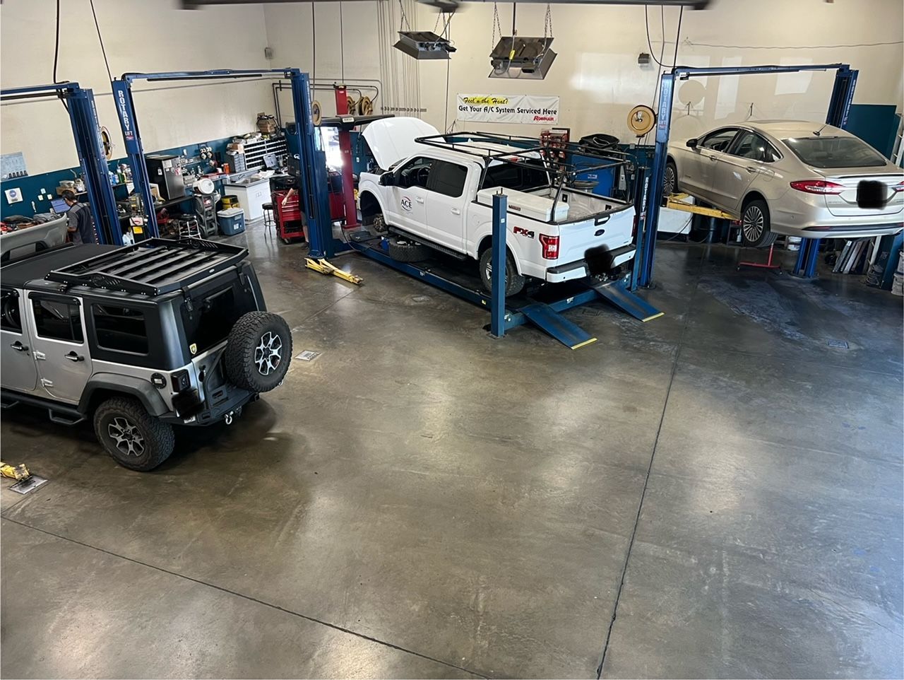 Auto repair shop with three vehicles on lifts and a Jeep parked on the floor