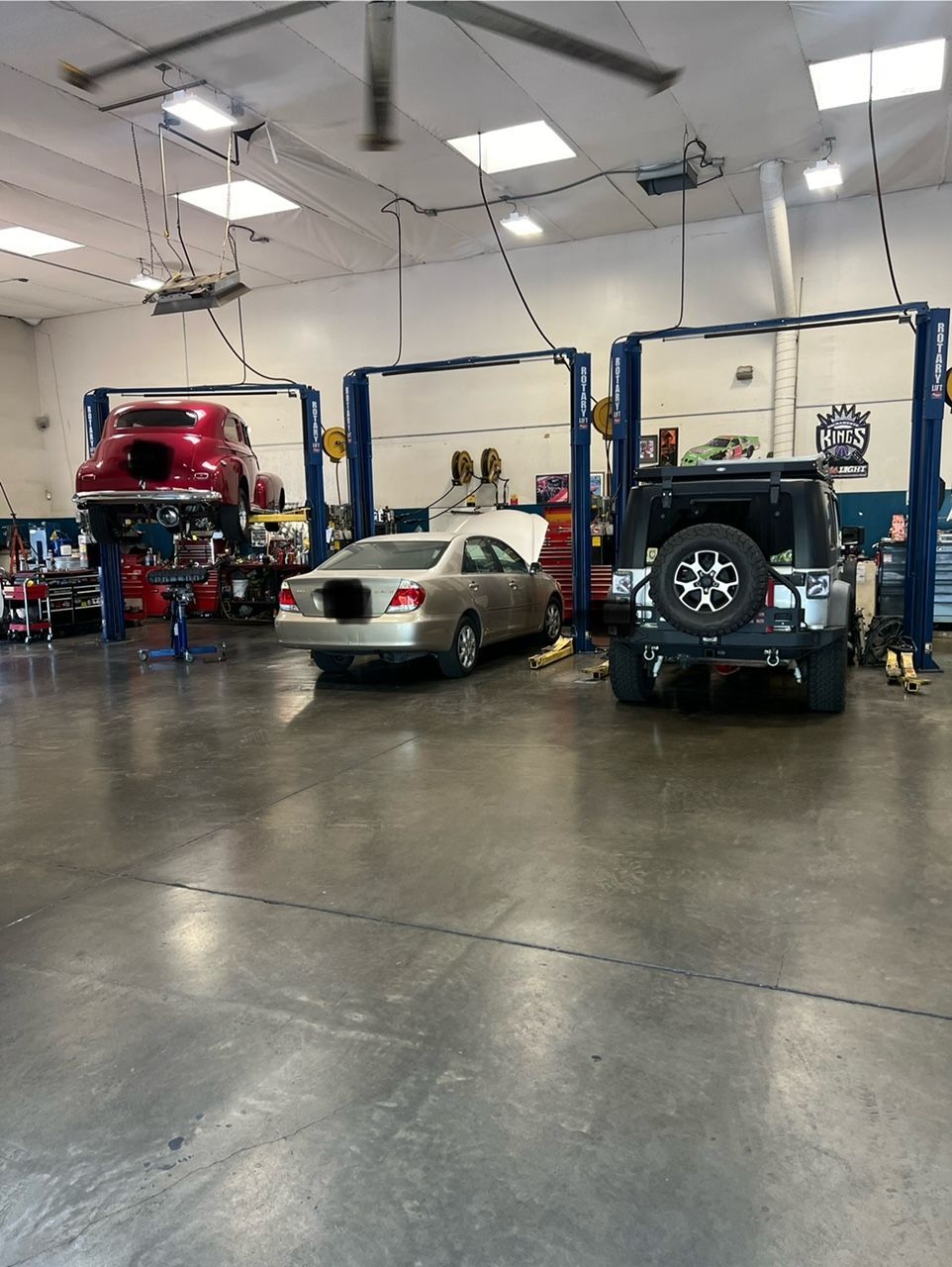 Auto repair shop with three vehicles on lifts and a silver sedan in the center bay