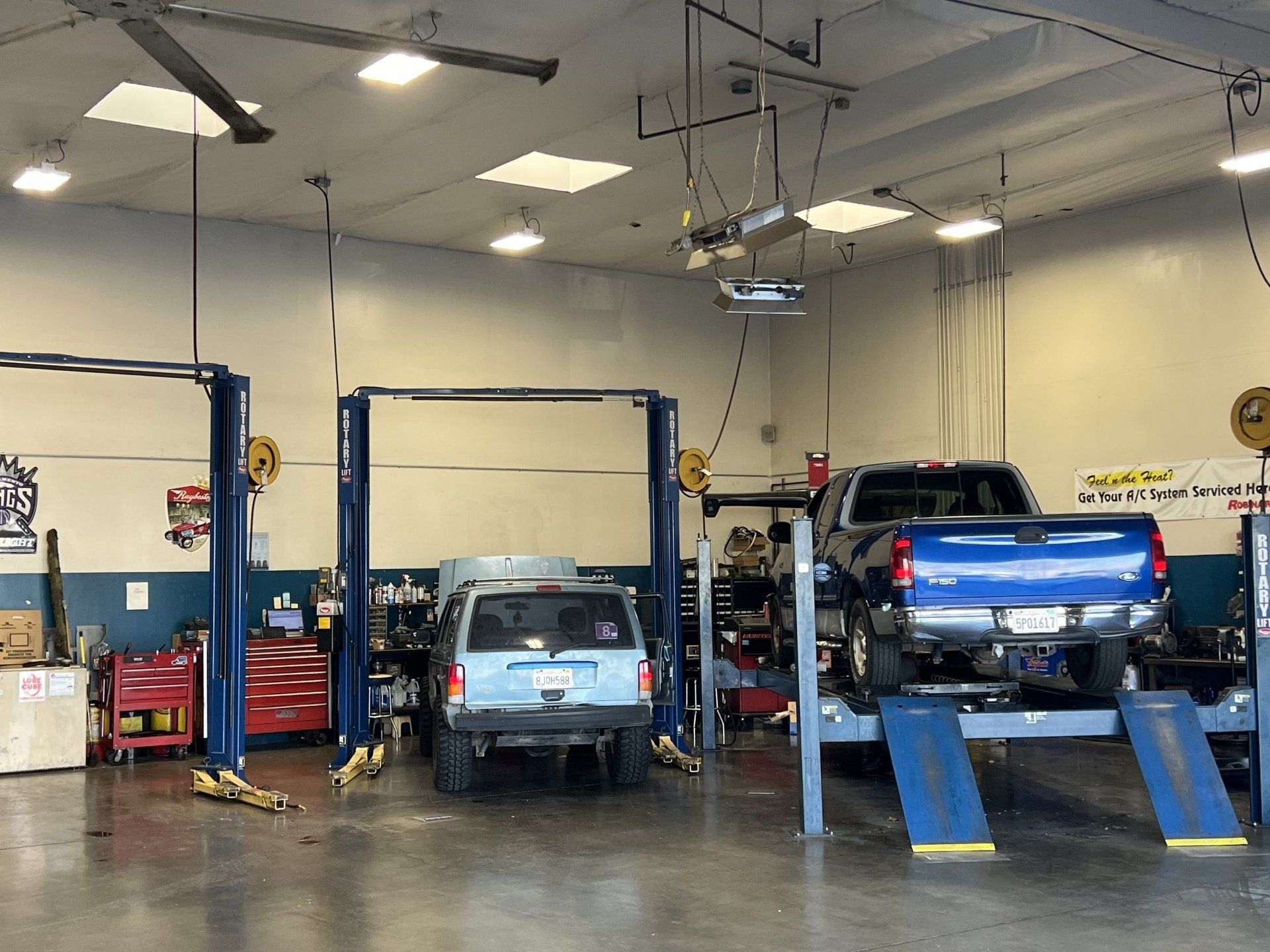 Auto repair shop with a small blue truck on a lift and a blue pickup on ramps in a garage bay