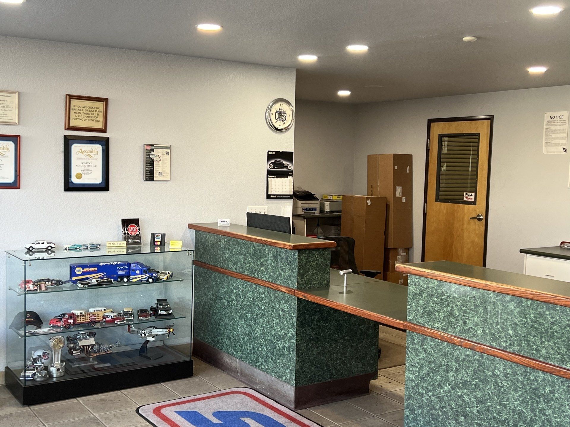 Small lobby with glass display case, reception desk, framed certificates, and wooden door.
