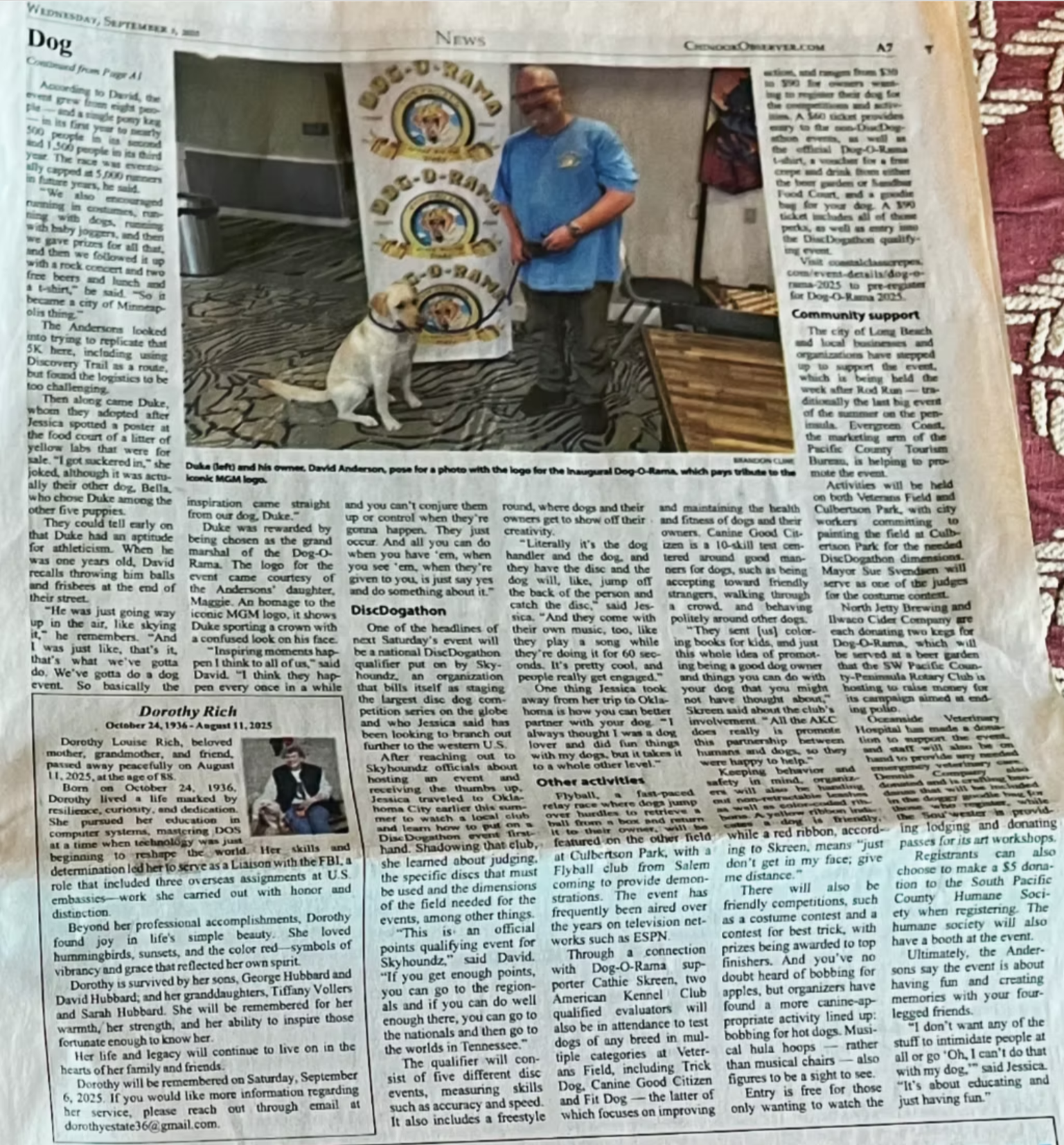 Newspaper page from the Chinook Observer with a large photo of a man and dog standing by a wall with circular logos.