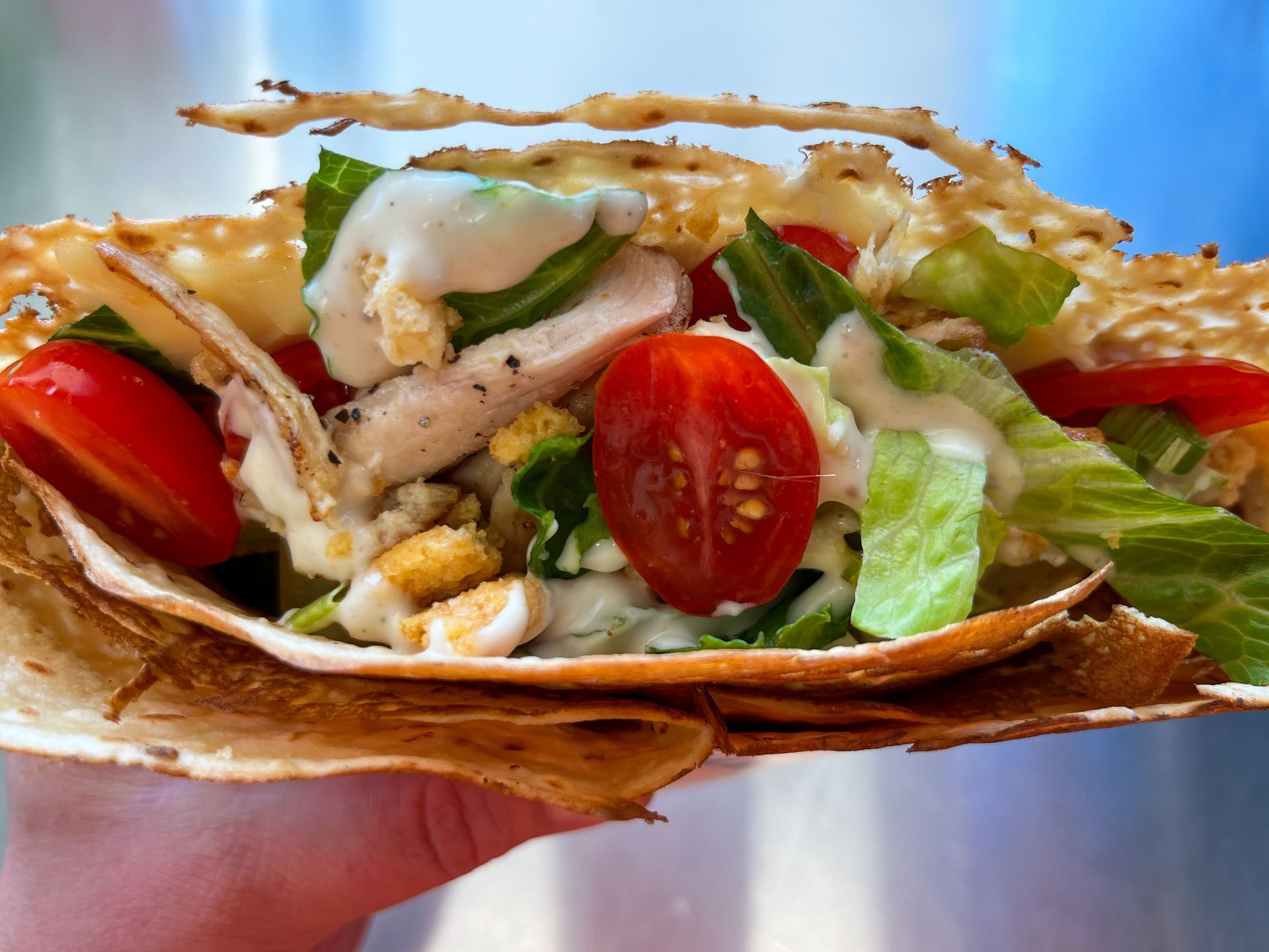 Hand holding a chicken taco with lettuce, tomato, and creamy sauce on a toasted tortilla.