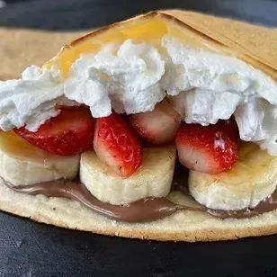 Crêpe dessert with whipped cream, strawberries, banana slices, and chocolate spread on a plate