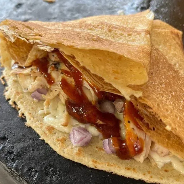 Grilled sandwich with melted cheese, diced onions, and sauce on a dark plate