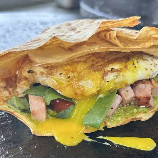 Flatbread sandwich with egg, melted yellow cheese, ham, and green peppers on a dark plate