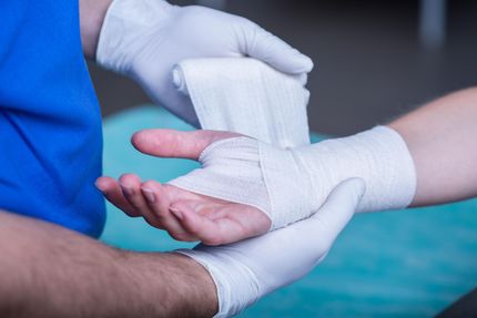 Two people wrapping a hand with white medical bandages during first aid.