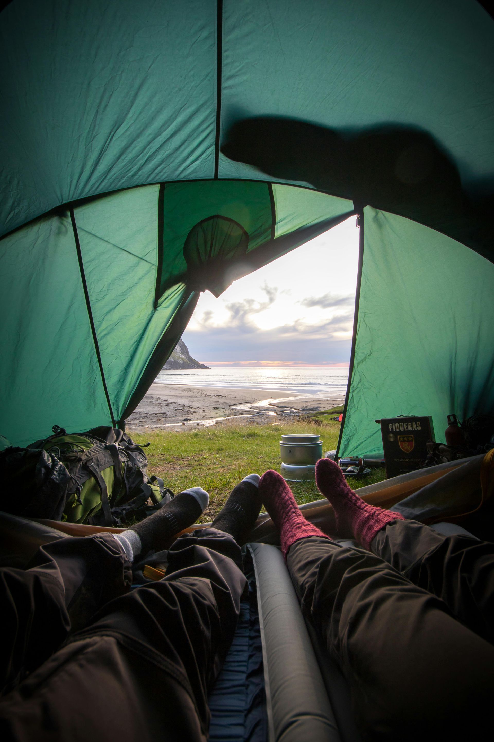 Vista desde el interior de una tienda de campaña hacia una playa, con dos pares de piernas, con calcetines, descansando.
