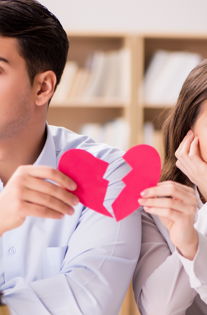 A man and a woman are sitting back to back holding a broken heart.