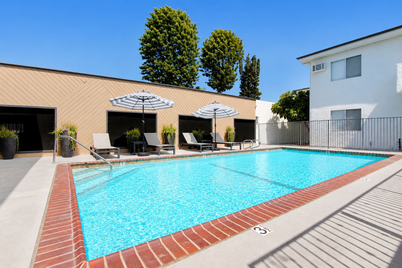 Outdoor swimming pool beside a beige motel with lounge chairs and umbrellas on a sunny day
