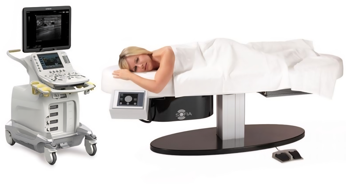 Medical ultrasound machine beside a patient lying on an exam table, receiving a scan