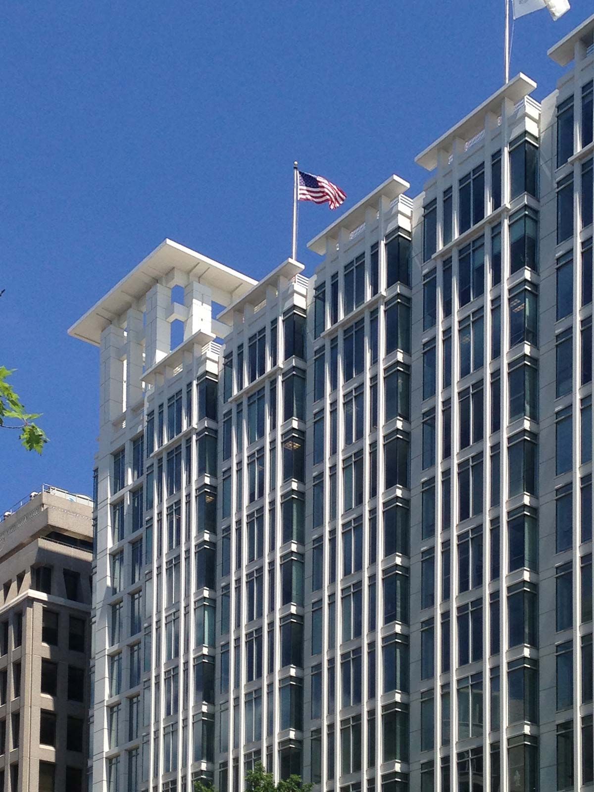 Tall modern glass building with an American flag flying against a clear blue sky