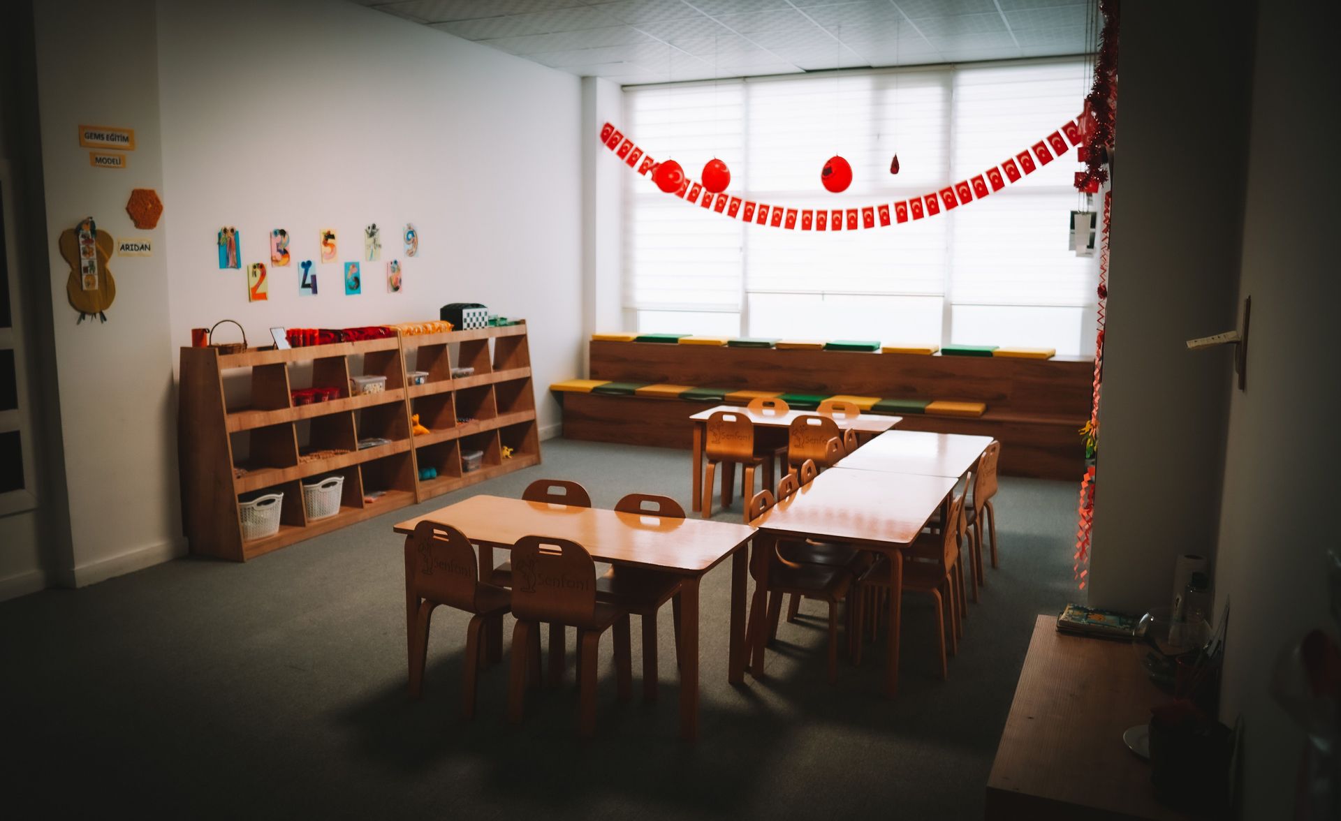Empty Head Start classroom with wooden tables, small chairs, cubbies, and red paper garland.
