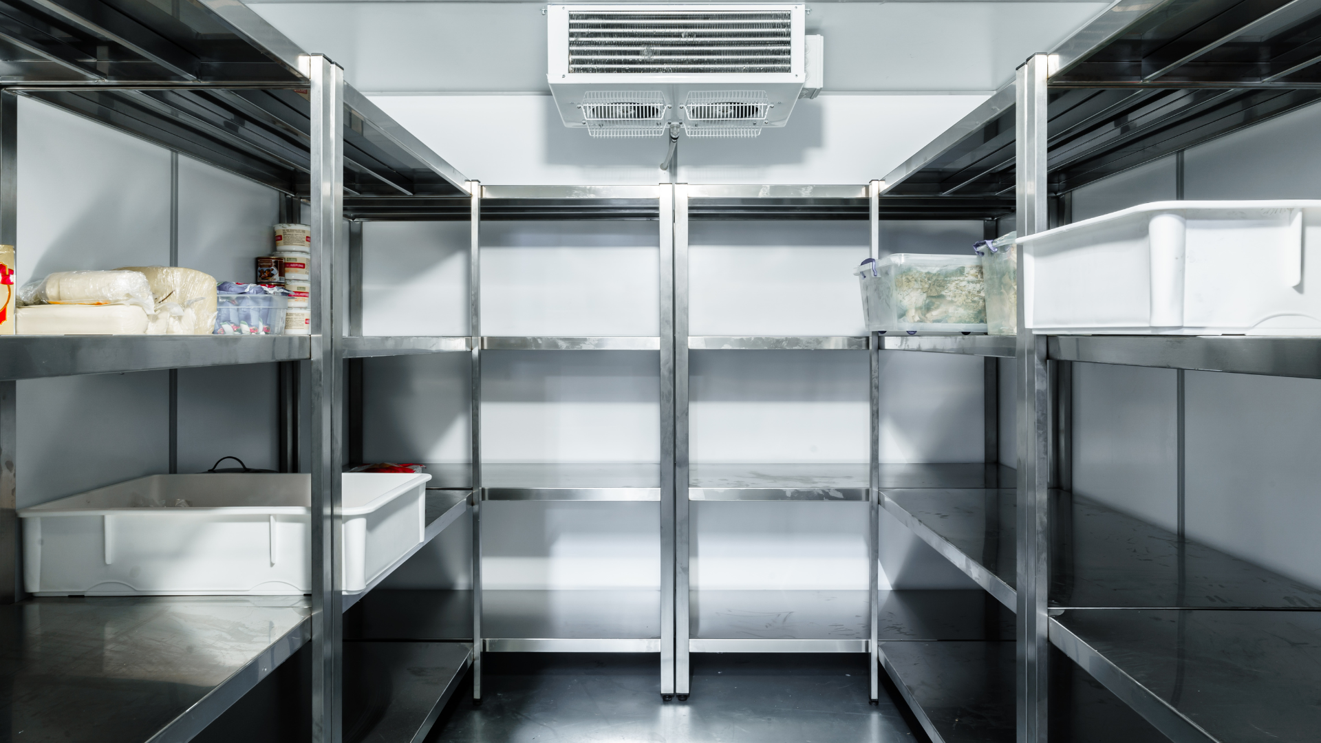 Empty stainless-steel walk-in refrigerator with metal shelves and white storage bins