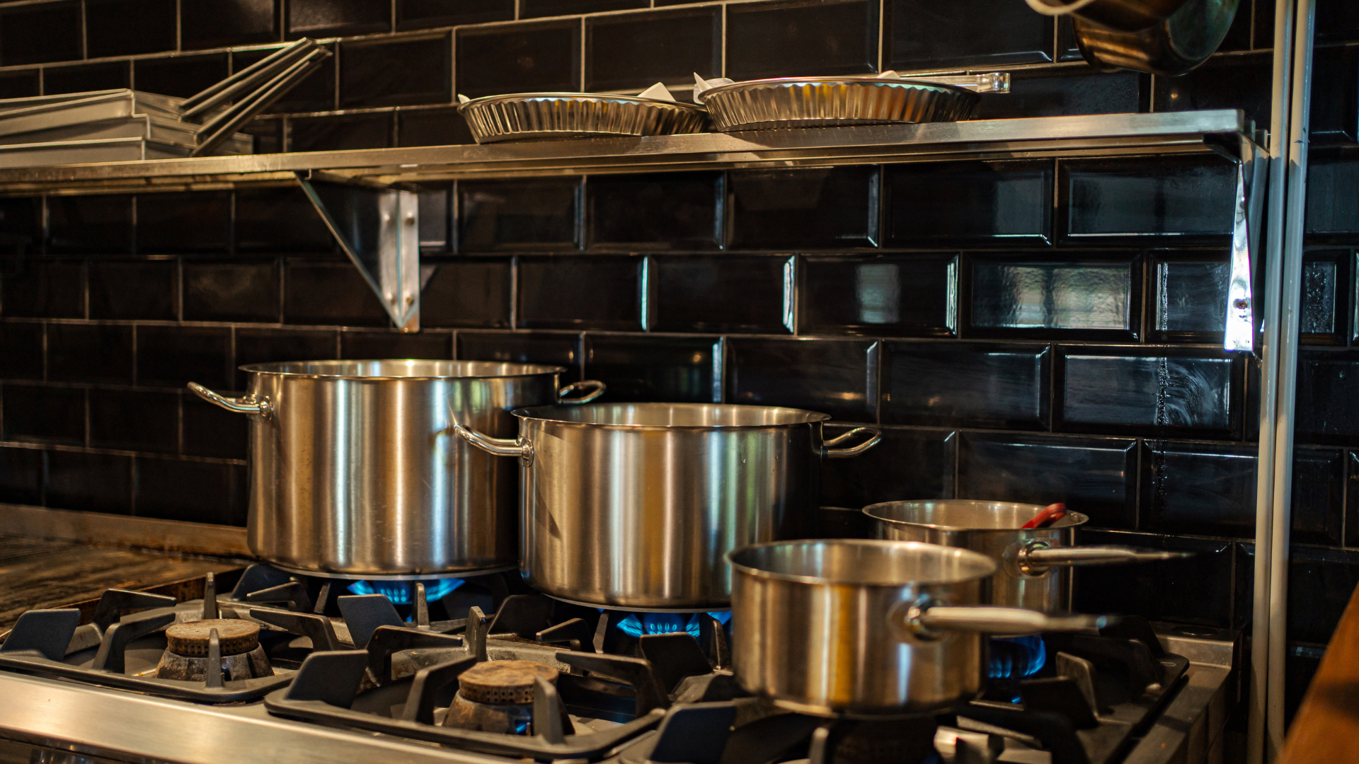 Three stainless steel pots on a gas stovetop in a kitchen with black tile backsplash