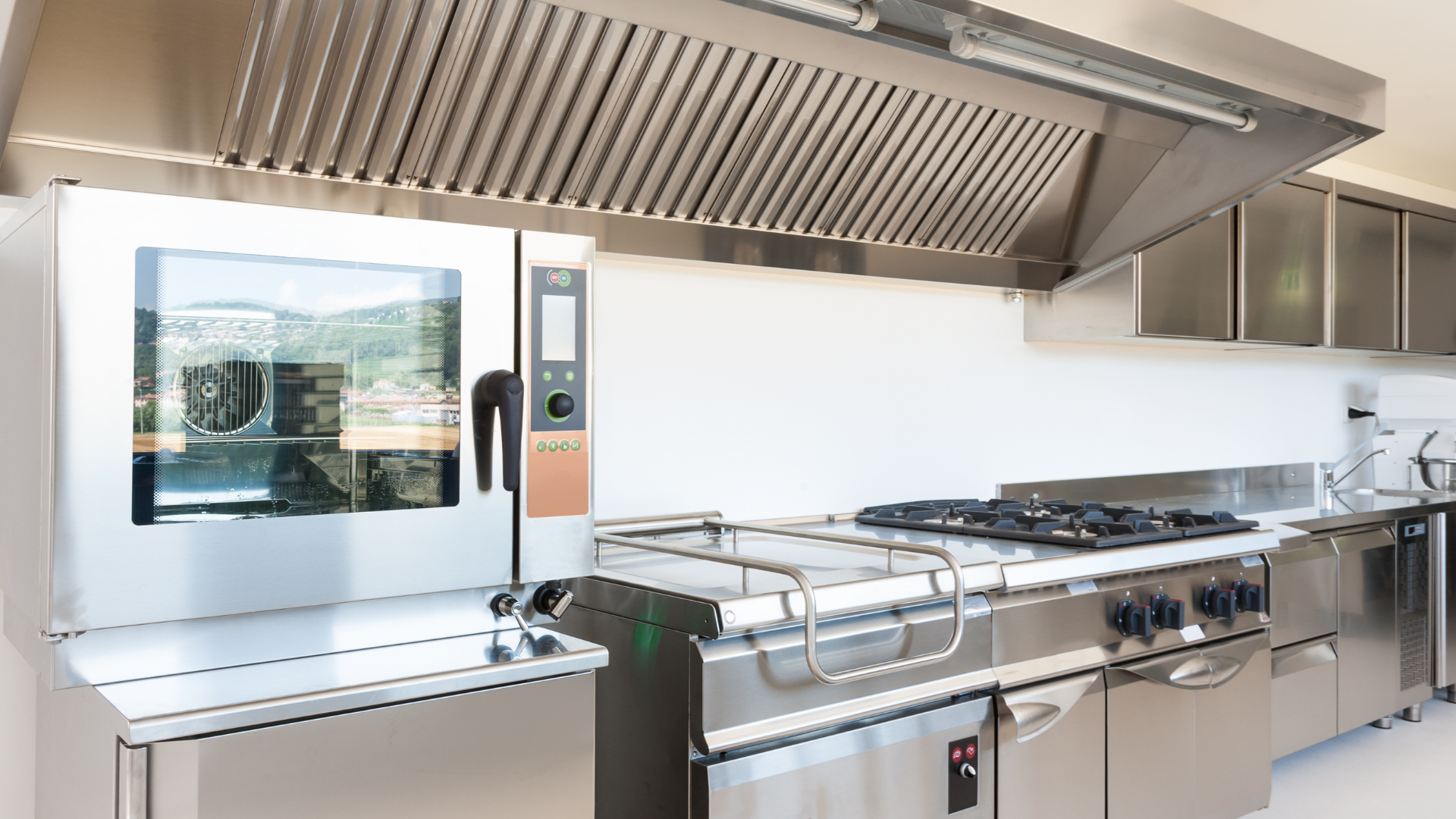 Commercial kitchen with stainless steel appliances, large oven, stove, and ventilation hood.