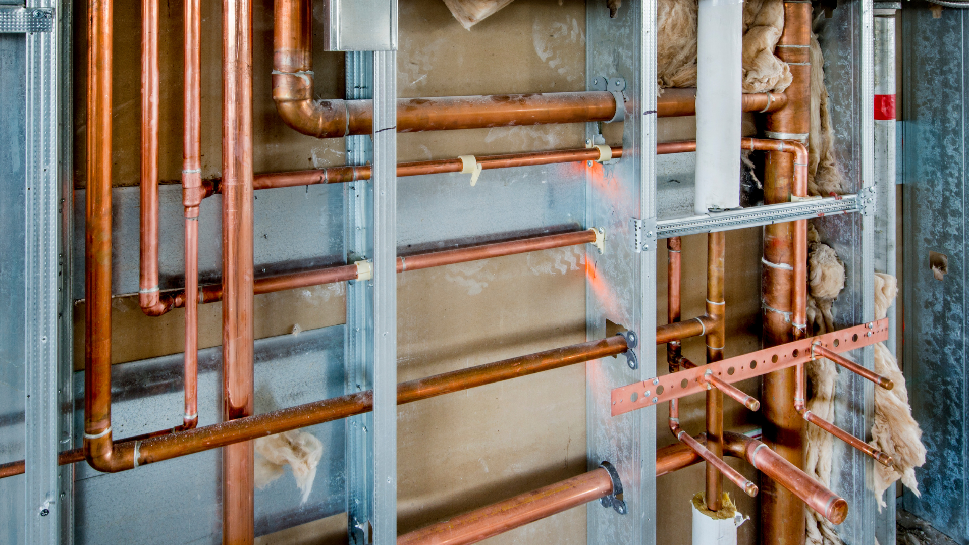 Exposed copper plumbing and pipes inside an unfinished wall framing under construction
