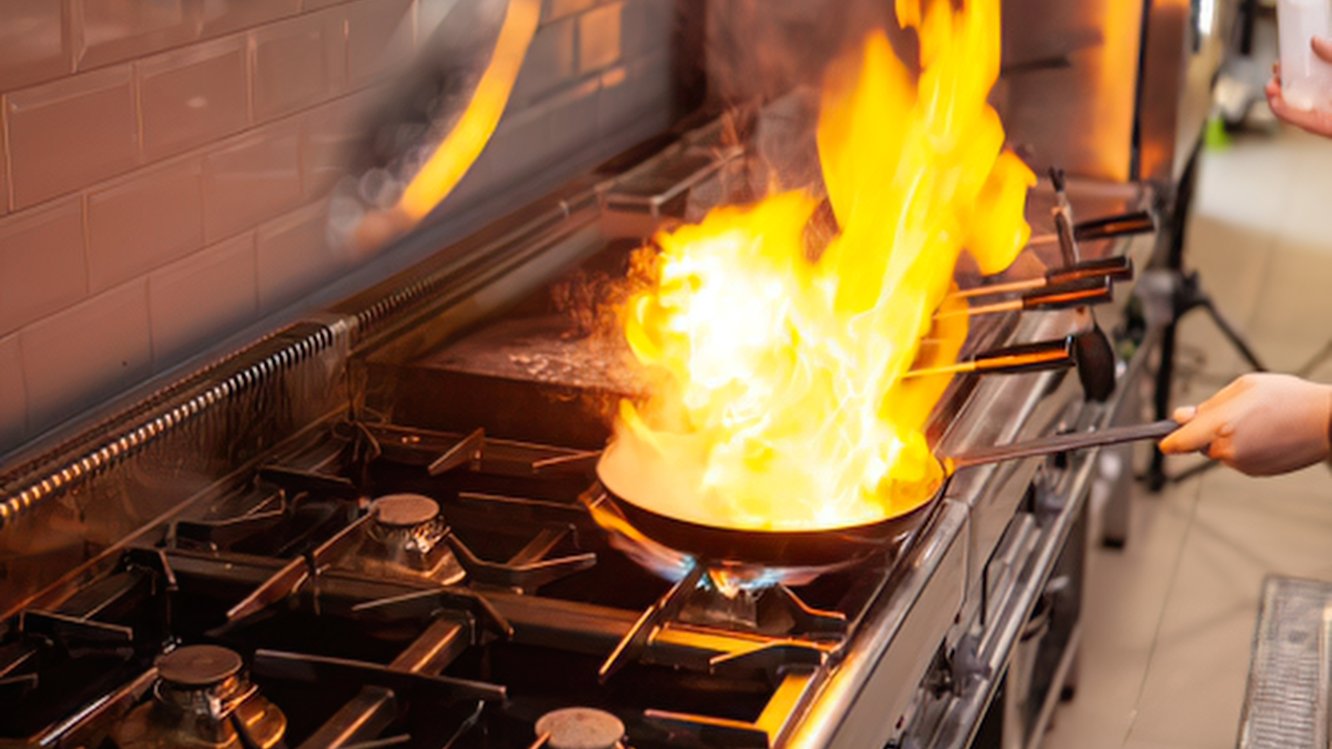 Chef cooking in a flaming pan on a gas stove in a commercial kitchen