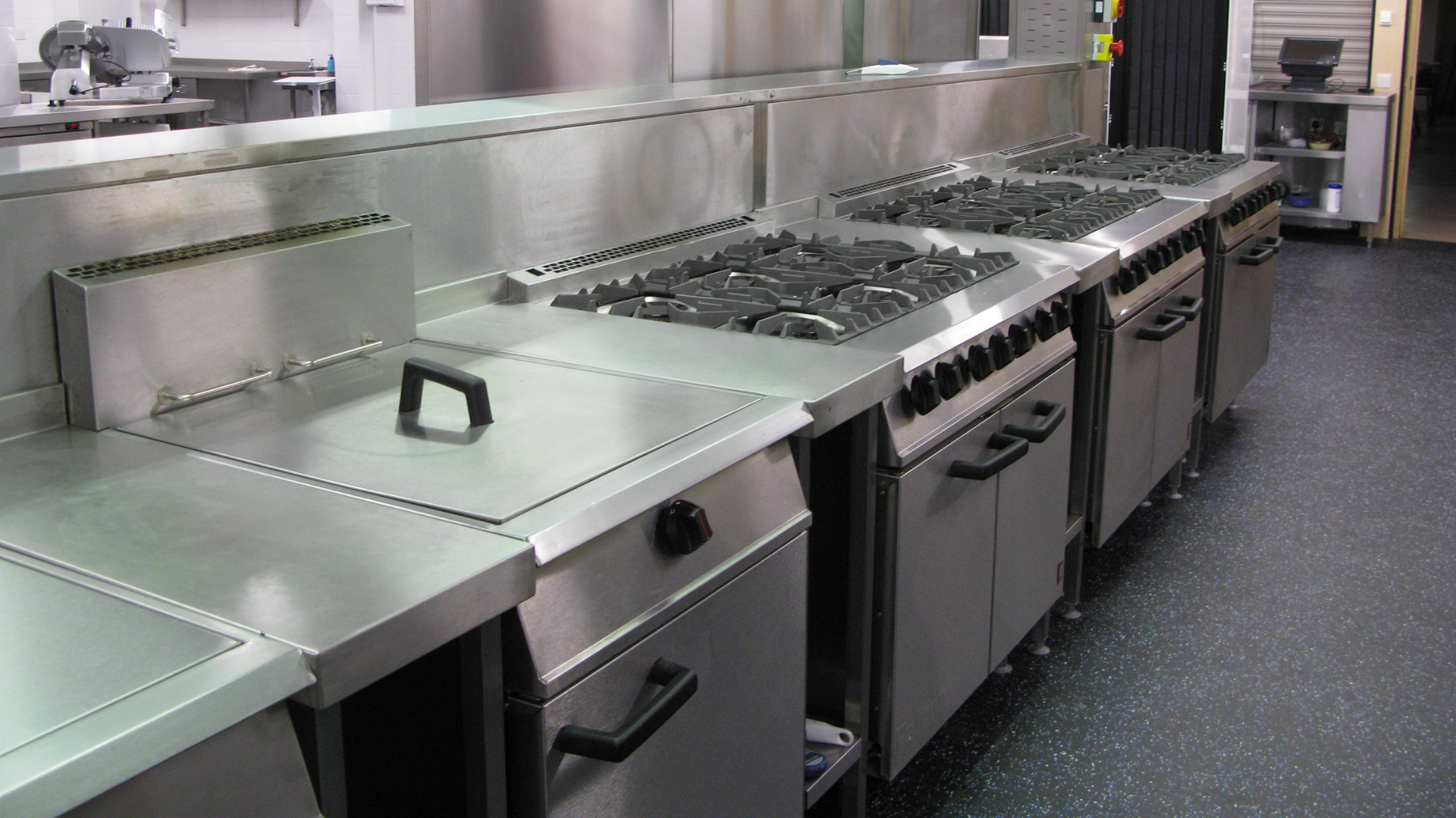 Commercial stainless-steel kitchen with multiple stoves and prep counters along the wall