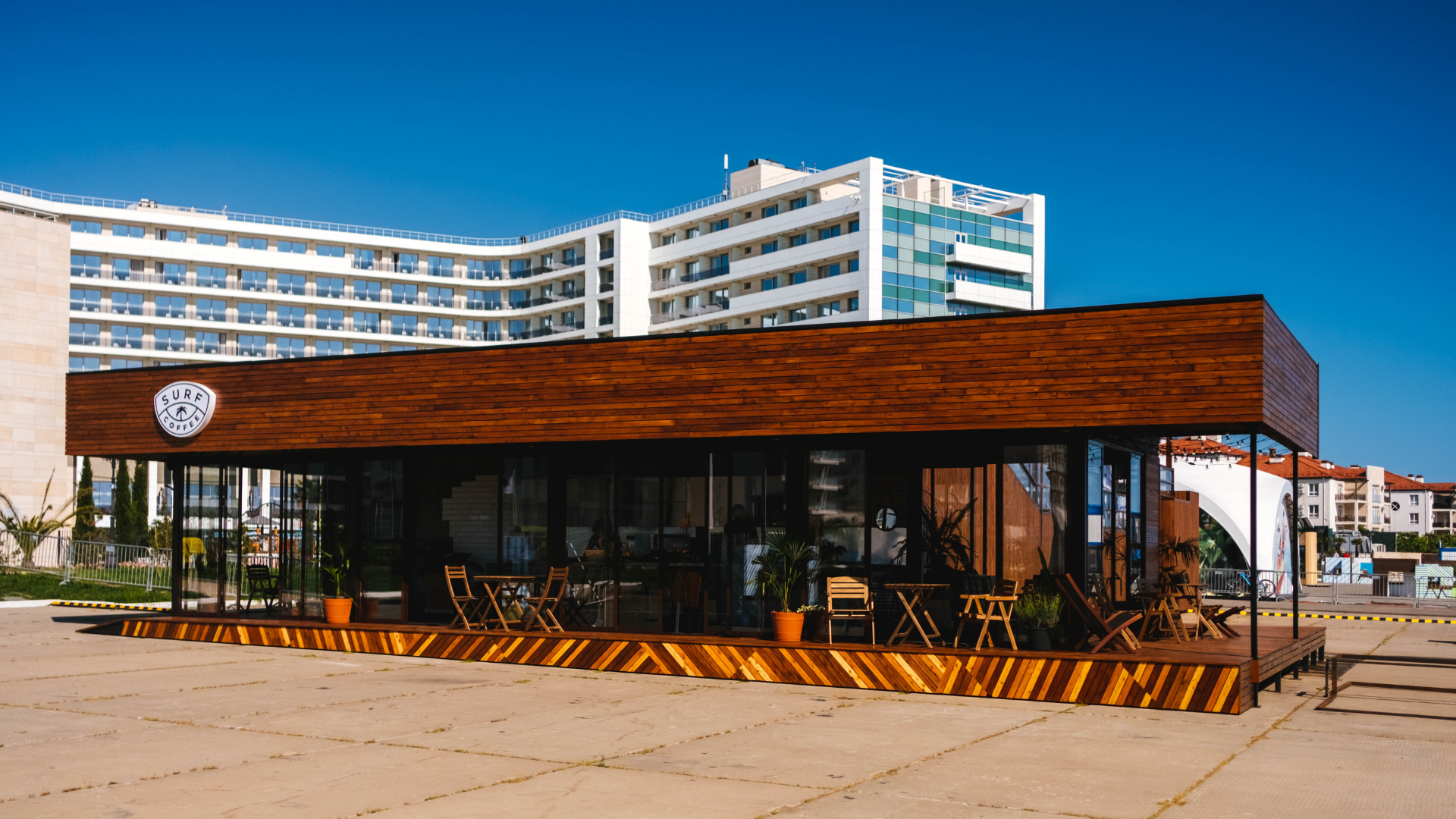Modern café with wood facade and outdoor seating in front of a large white building