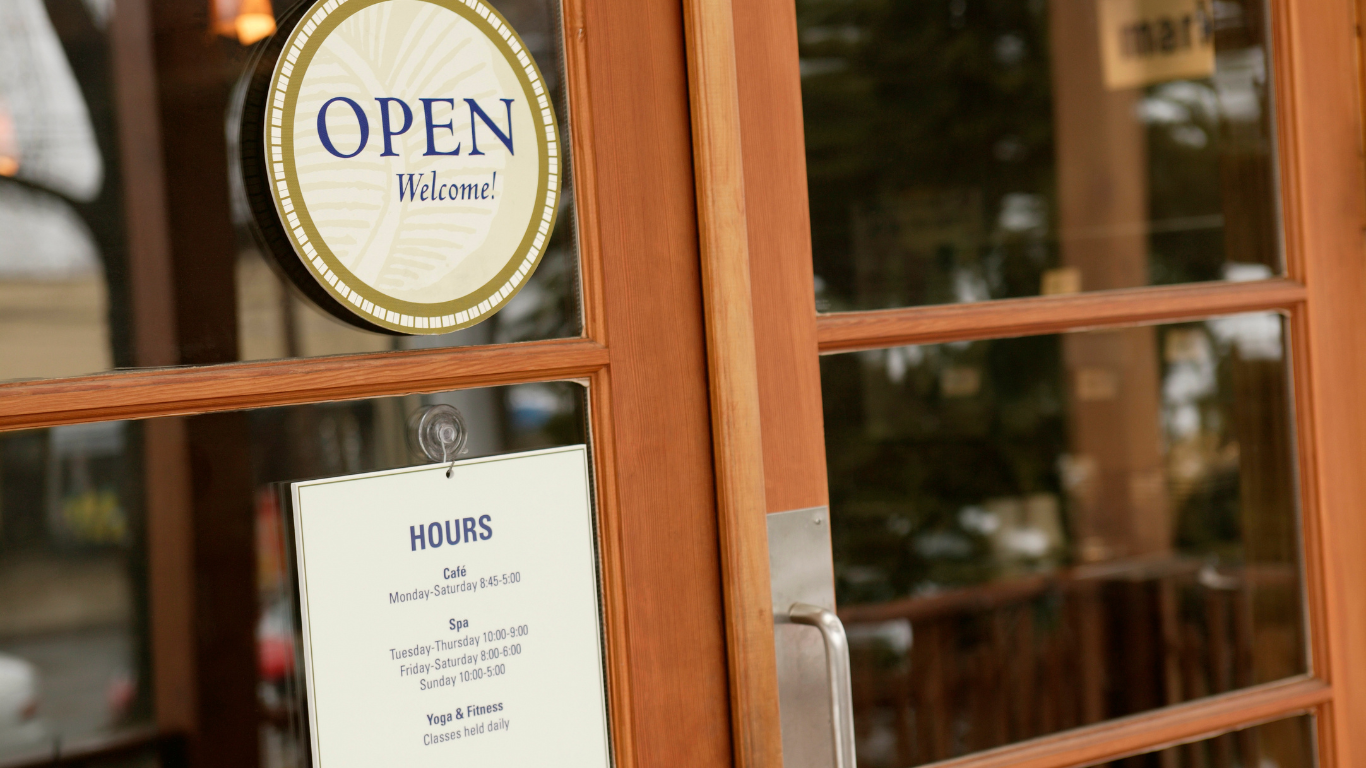 Wooden storefront door with an “OPEN” sign and a posted hours notice.