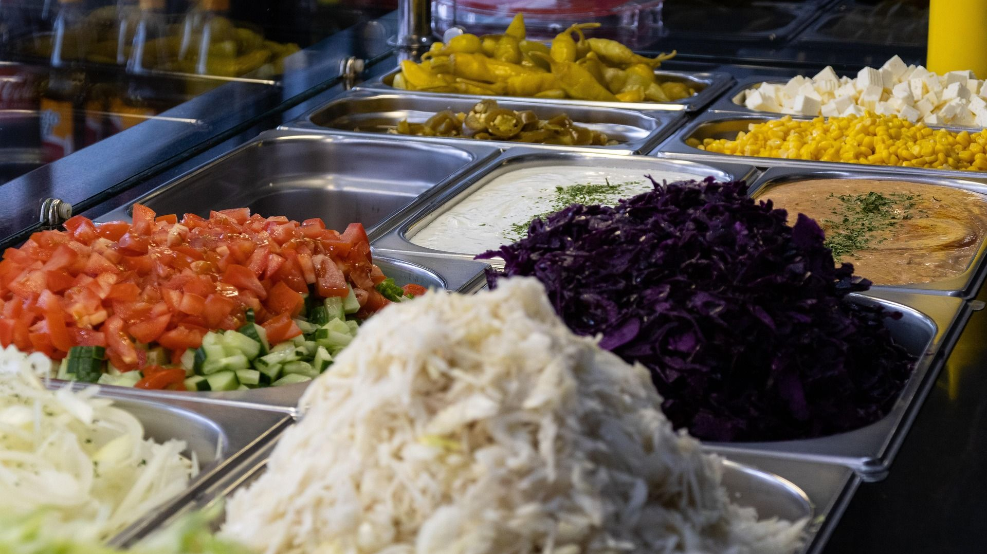 A counter with various toppings: diced tomatoes, cabbage, and sauces, likely at a restaurant.