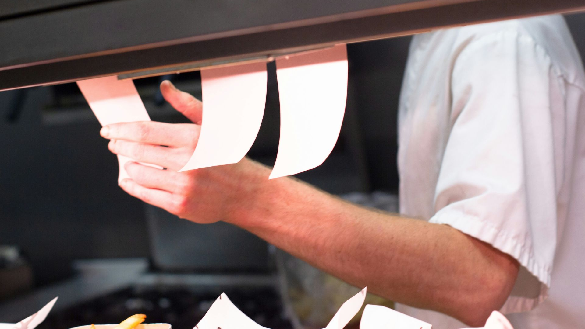 Person in a white shirt holding a large white sign behind a counter.