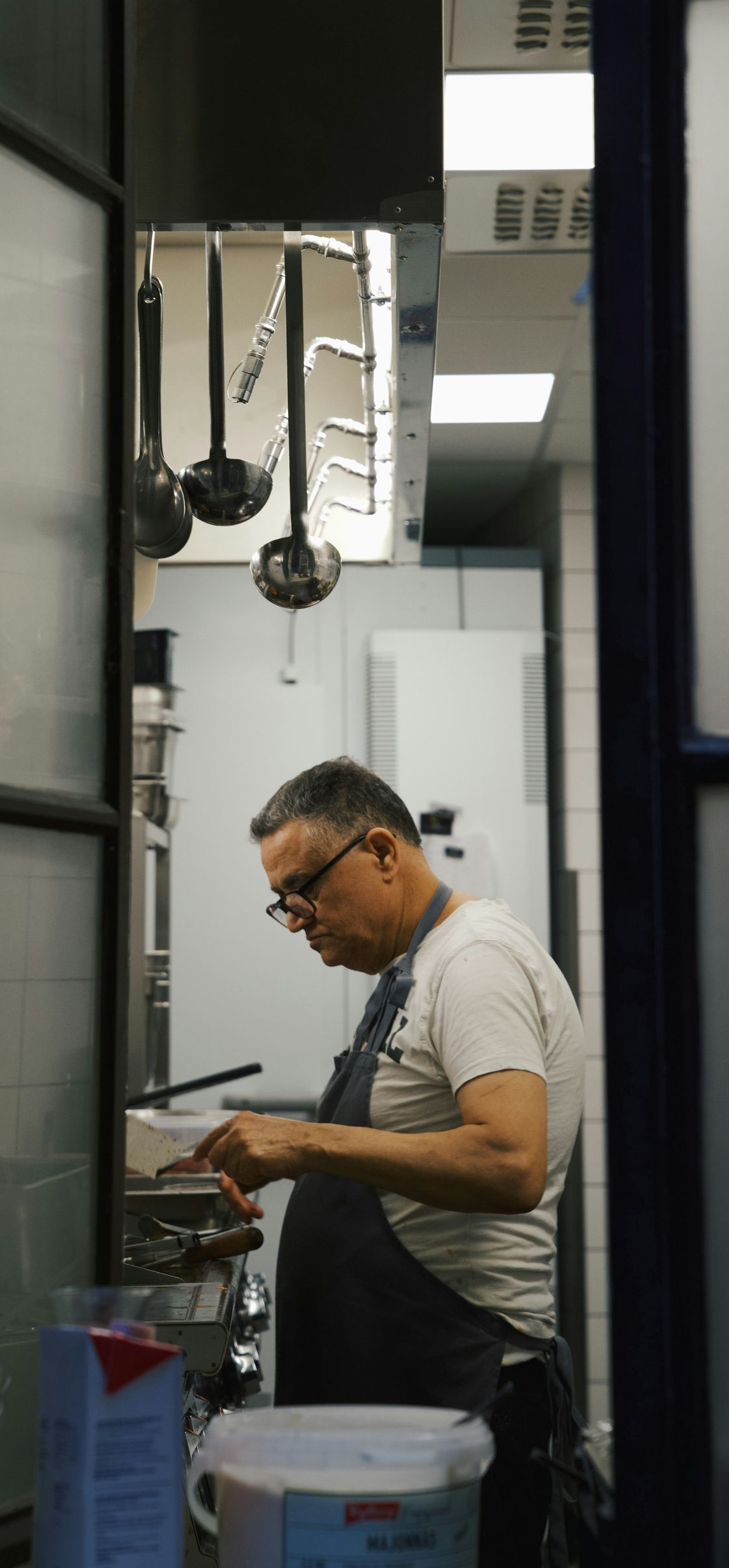 Person working at a bench in a lab or workshop, wearing glasses and a gray shirt.