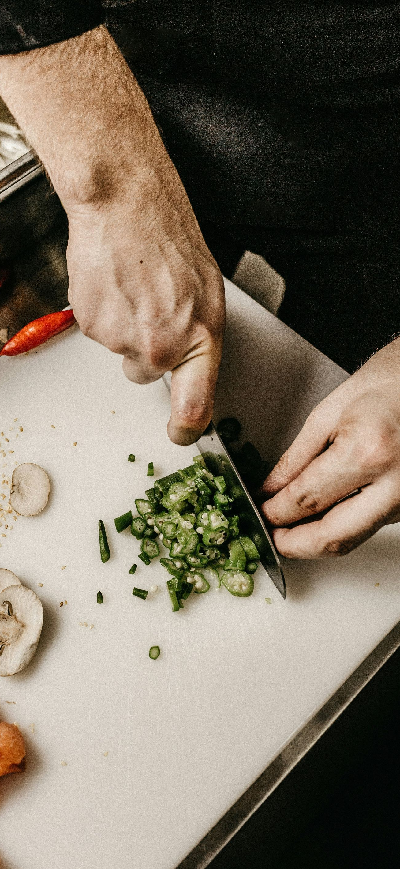 Hands chopping green herbs on a cutting board beside sliced mushrooms and shrimp.