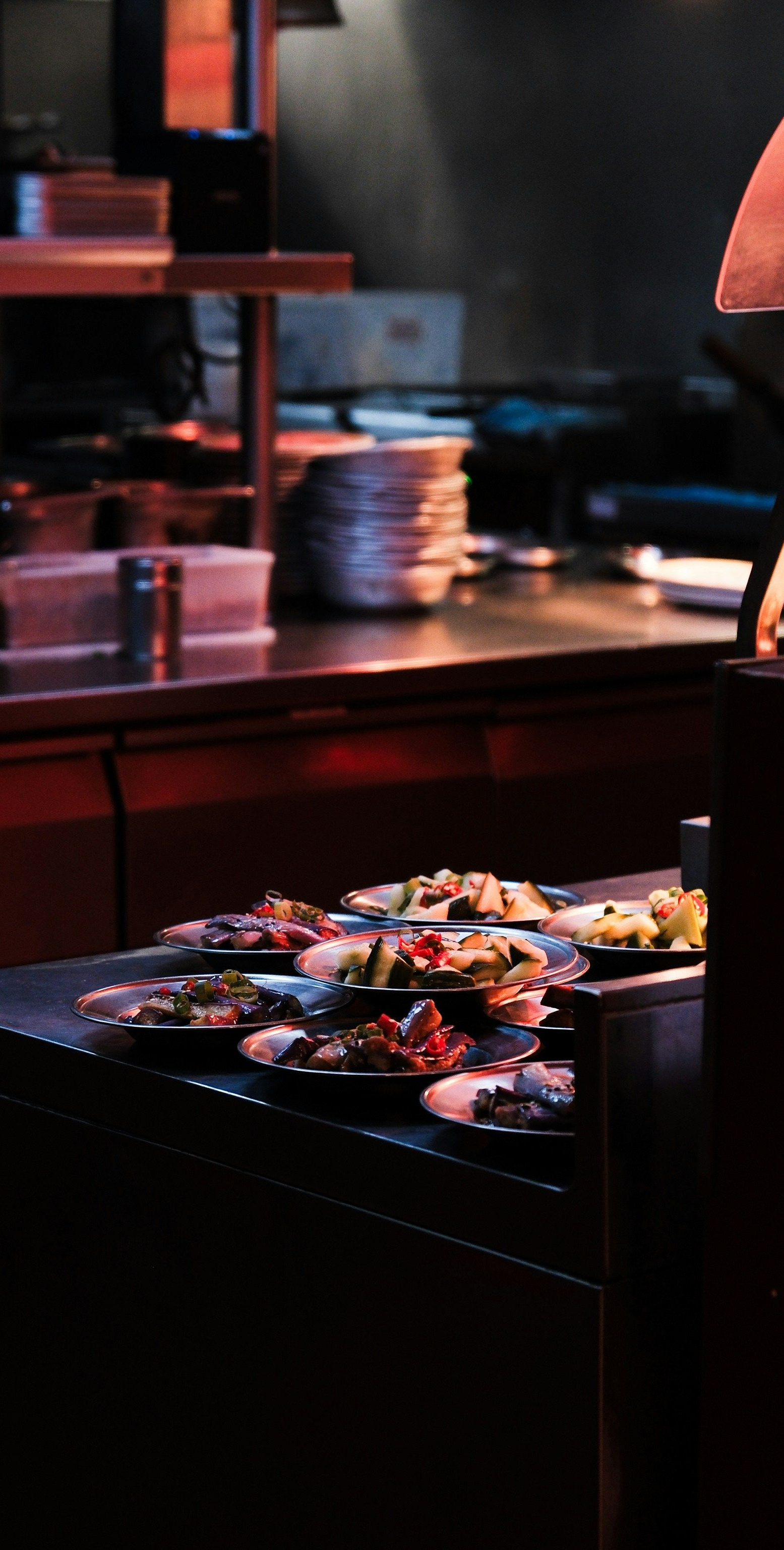 Dimly lit sushi bar with a tray of assorted sushi in the foreground and stacked plates behind it