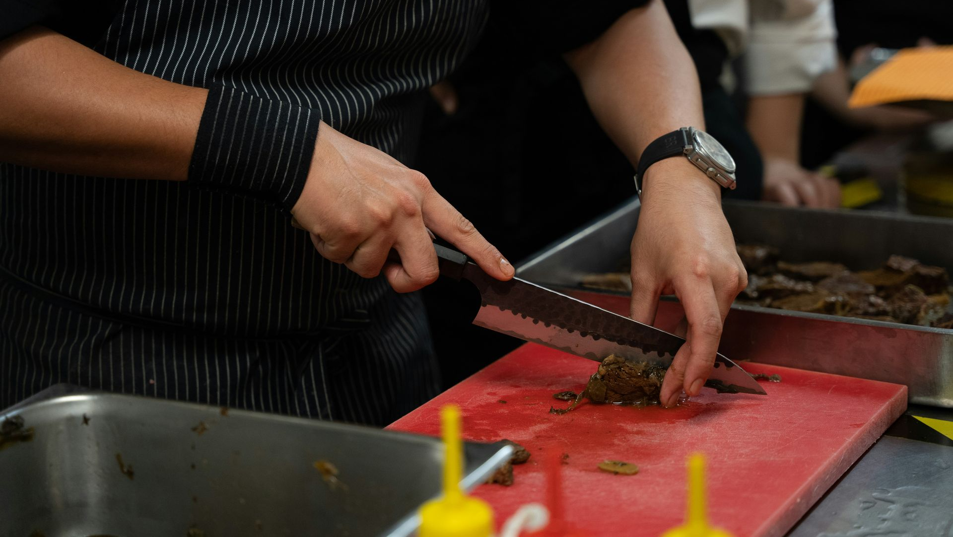 Cook slicing meat on a red cutting board in a kitchen prep area