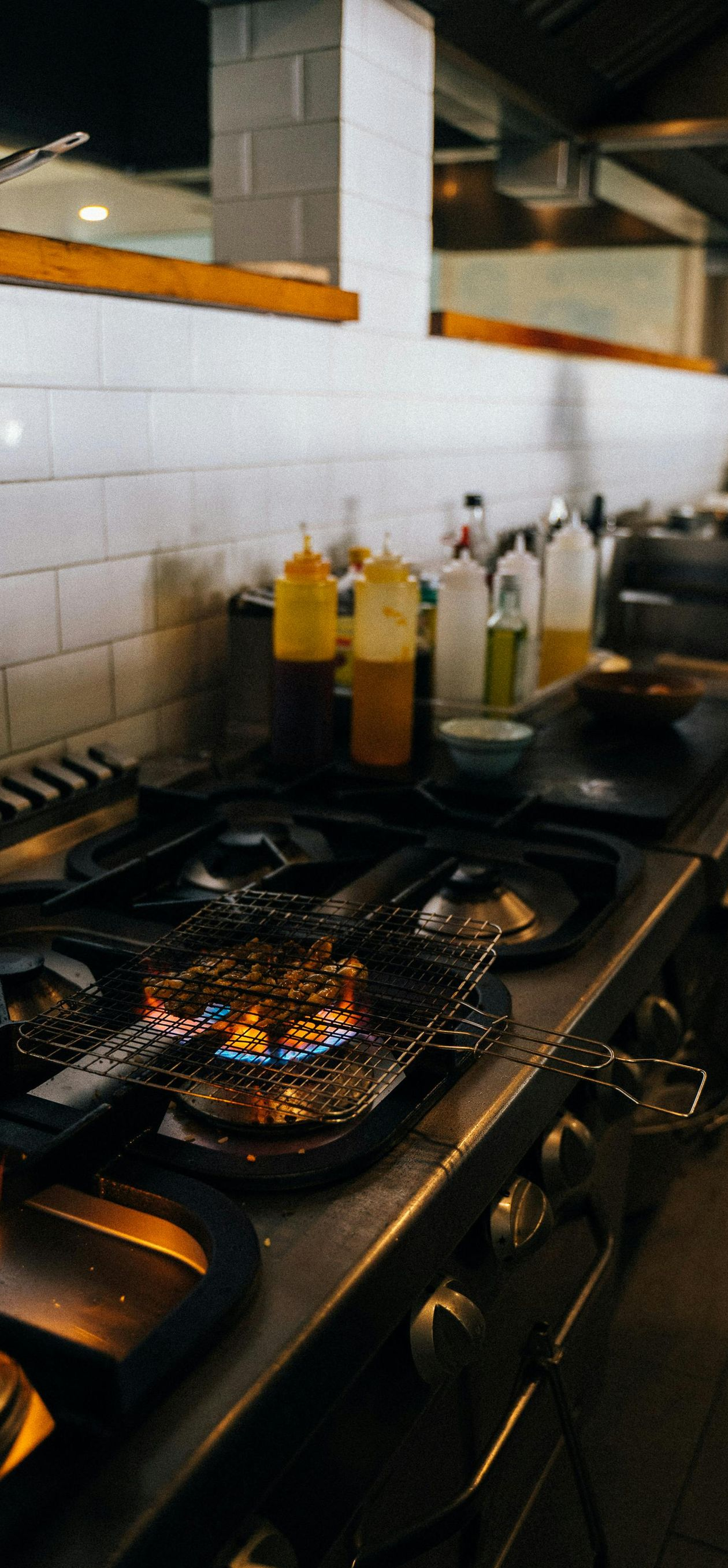 A dirty kitchen stove with a flame lit. Various bottles sit on the counter in the background.