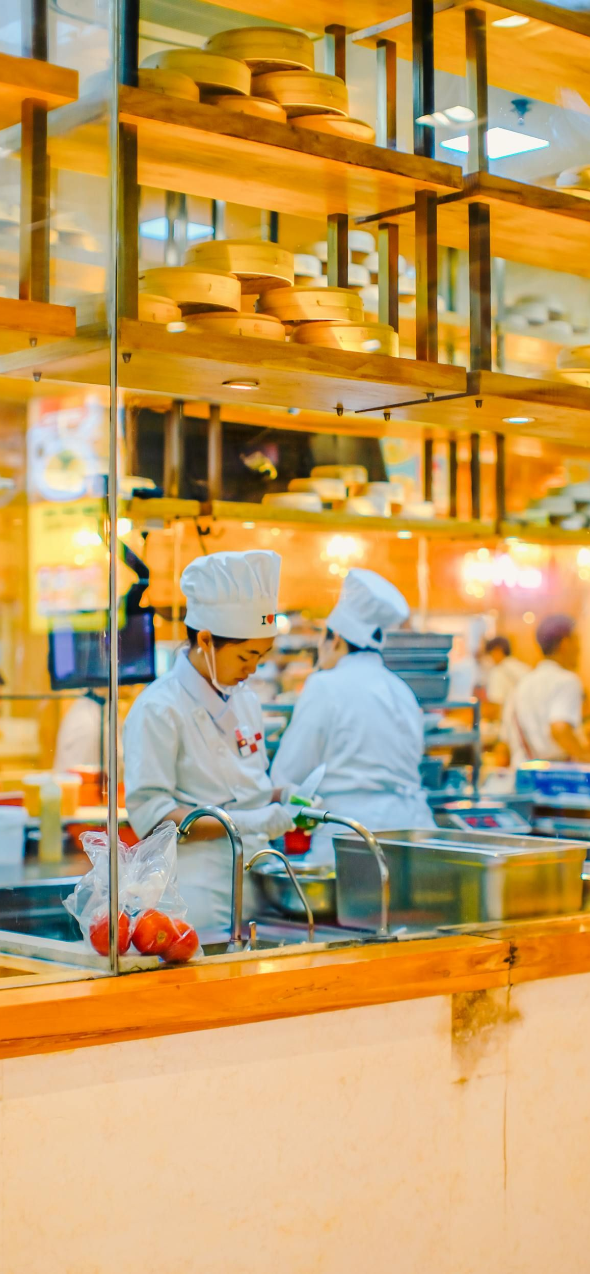 Chefs in white uniforms working in a bright open kitchen with copper lights and stainless steel counters