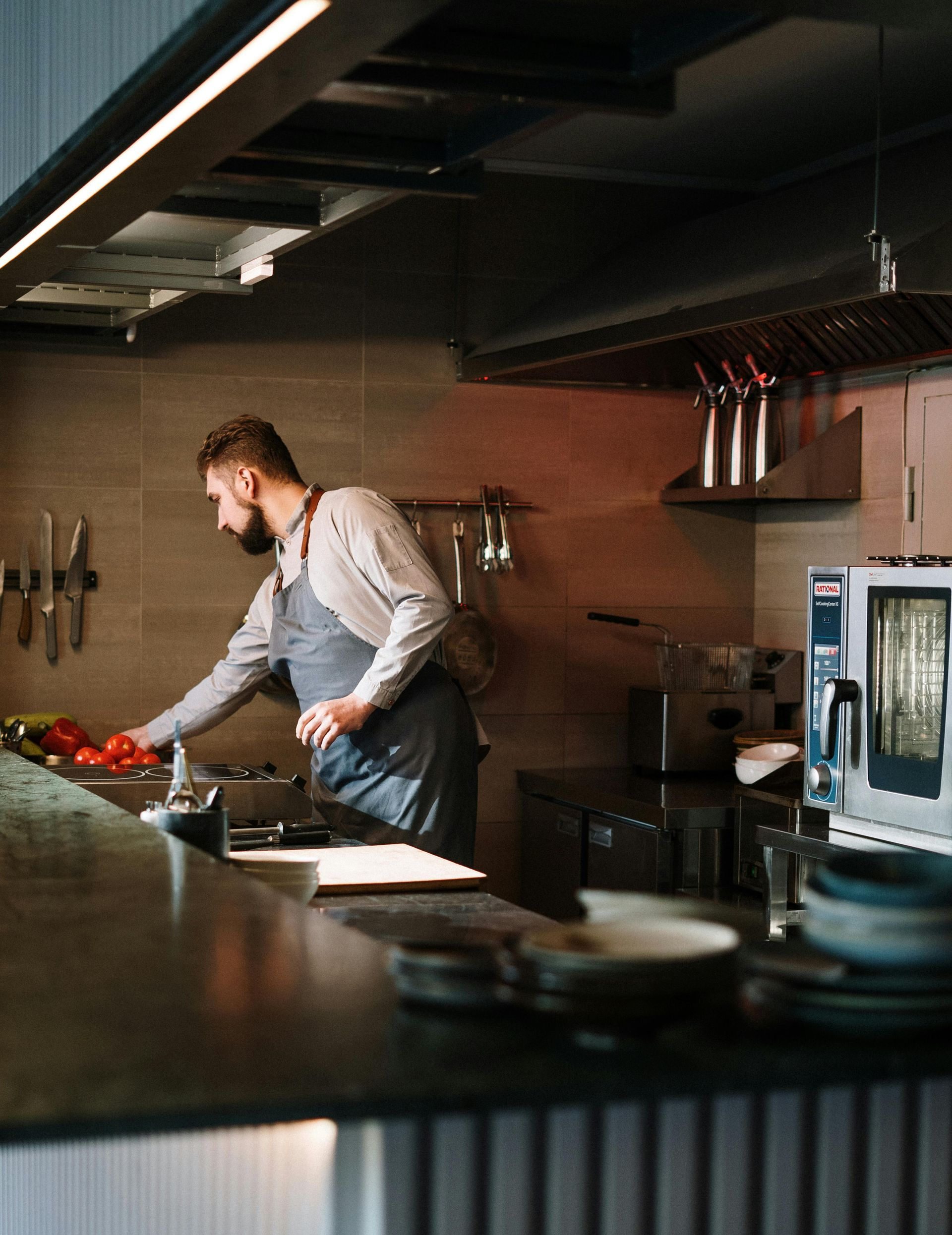 A person wearing an apron prepares ingredients on a counter in a dimly lit, professional restaurant kitchen.