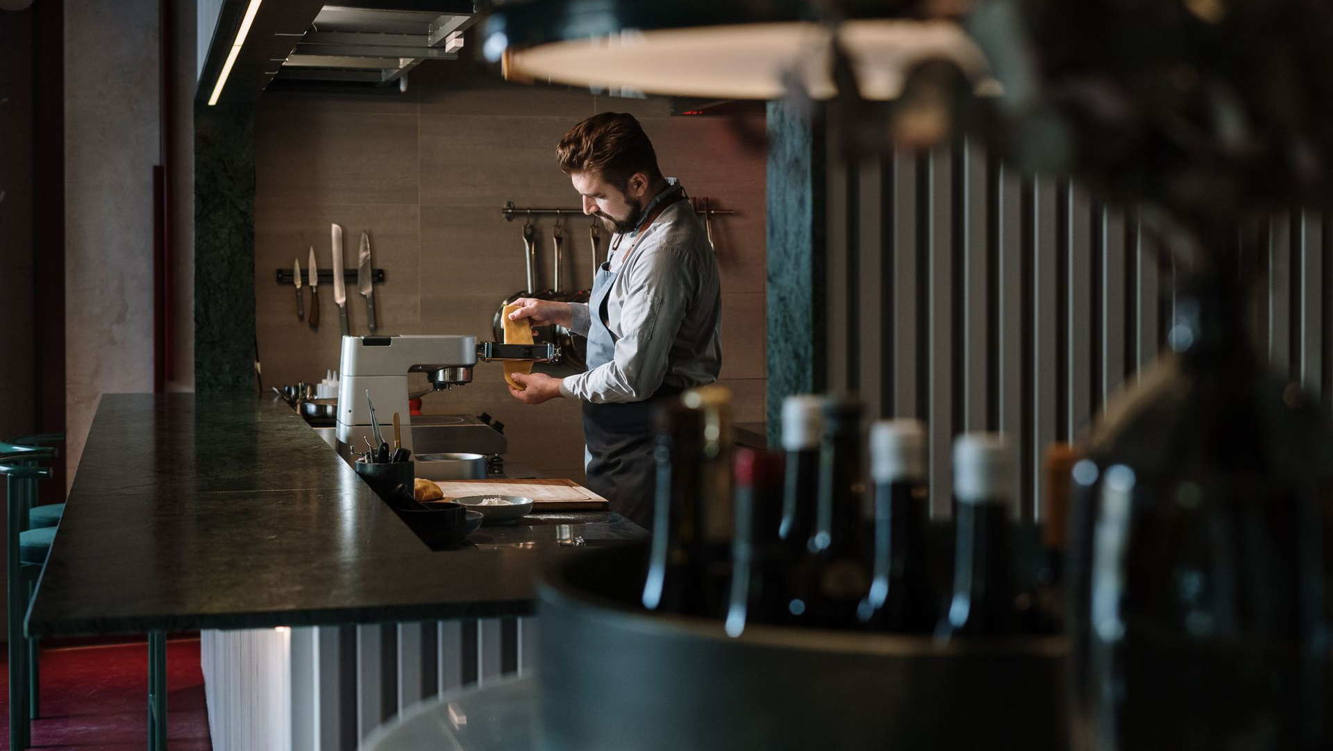 Person working behind a bar in a dimly lit café, surrounded by bottles and brewing equipment.