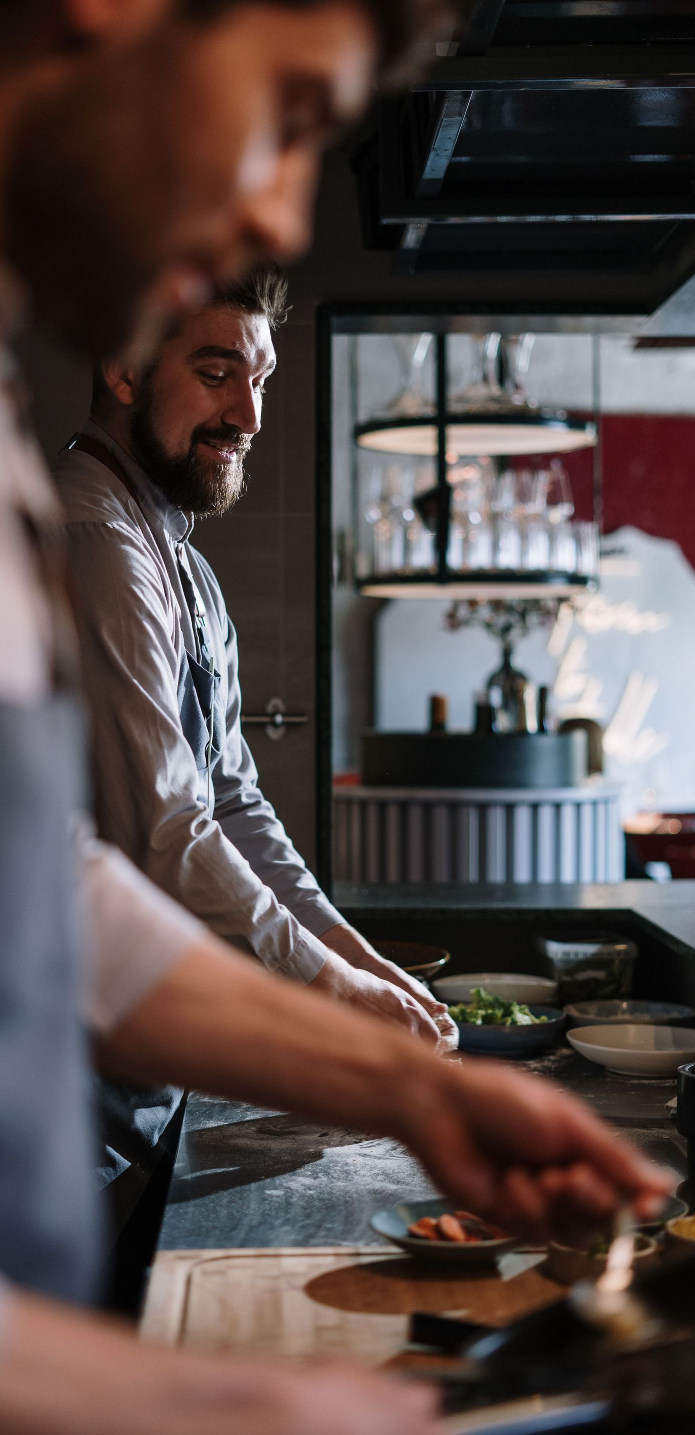 Chefs preparing food at a restaurant counter, with one focused on cooking in the foreground