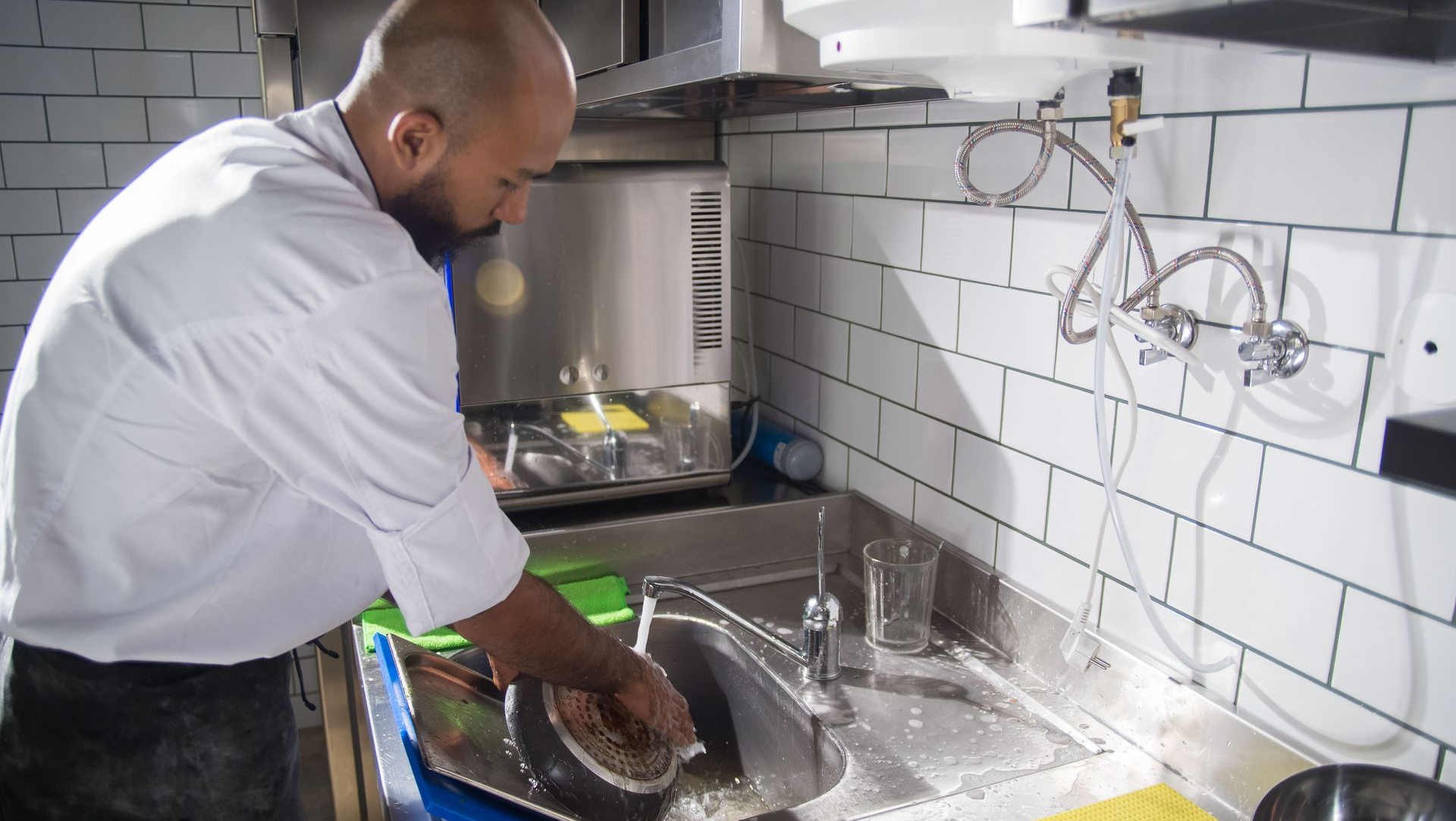 Person washing dishes in a kitchen sink with soap and running water