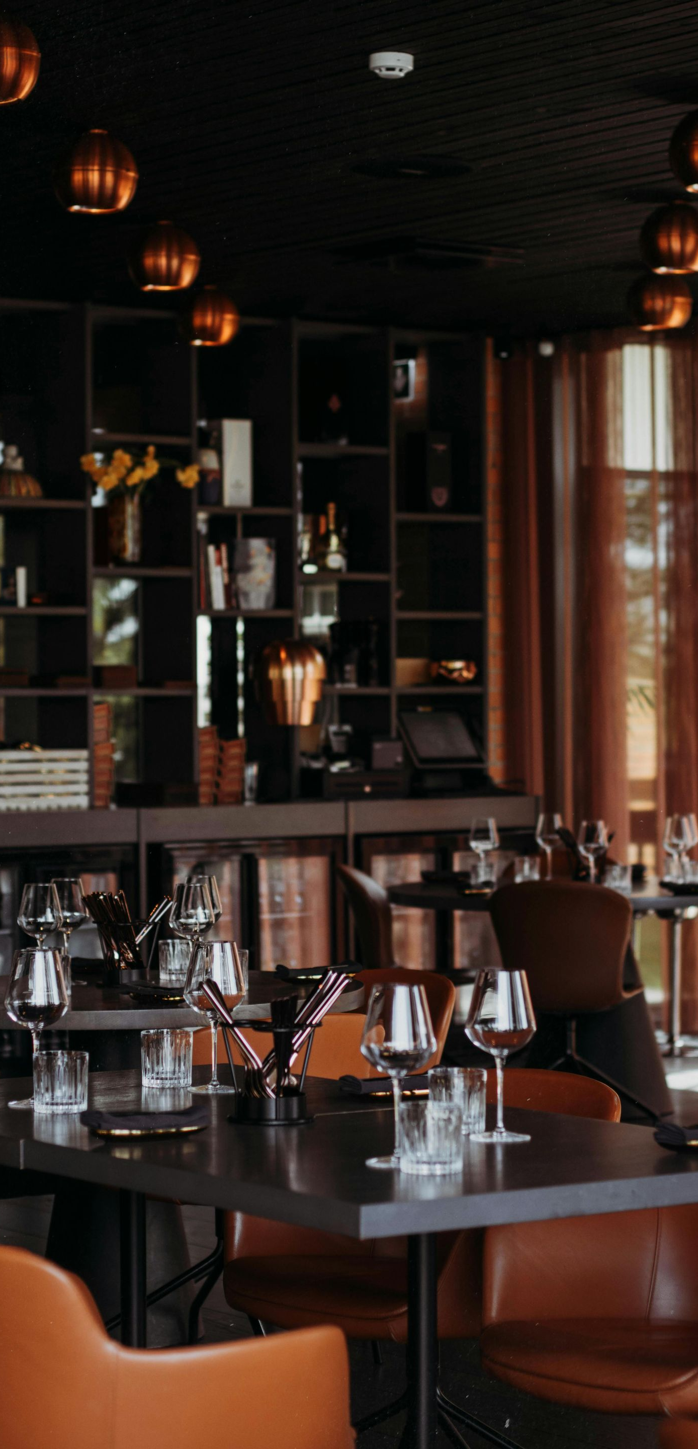 Elegant restaurant interior with dark wood tables, orange chairs, and warm pendant lighting