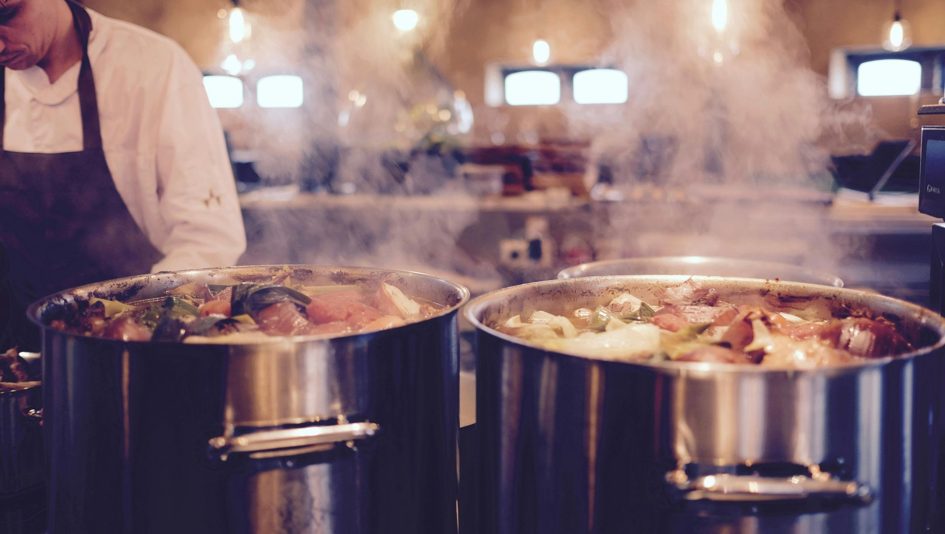 Chef in kitchen preparing food in steaming pots.