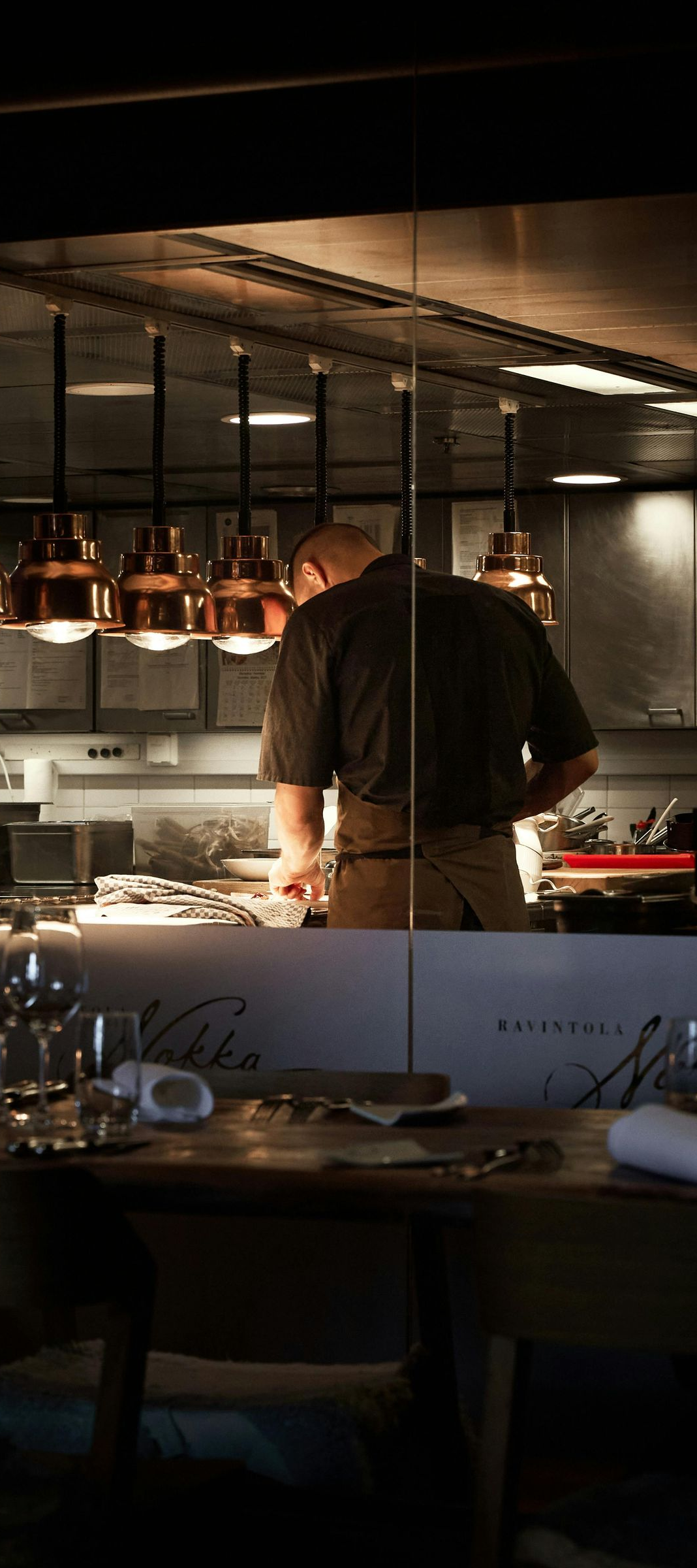 Chef working in a warm-lit restaurant kitchen beside hanging copper pans